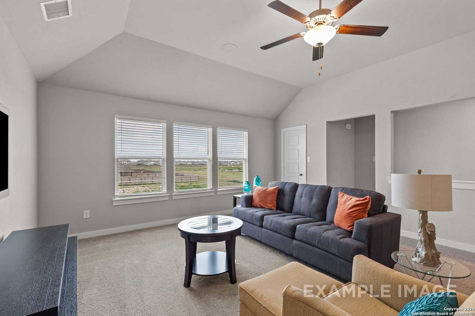 Cozy living room with vaulted ceiling, ceiling fan, large windows overlooking fields, gray sectional sofa in The Collin A, Davidson Homes, Seguin TX