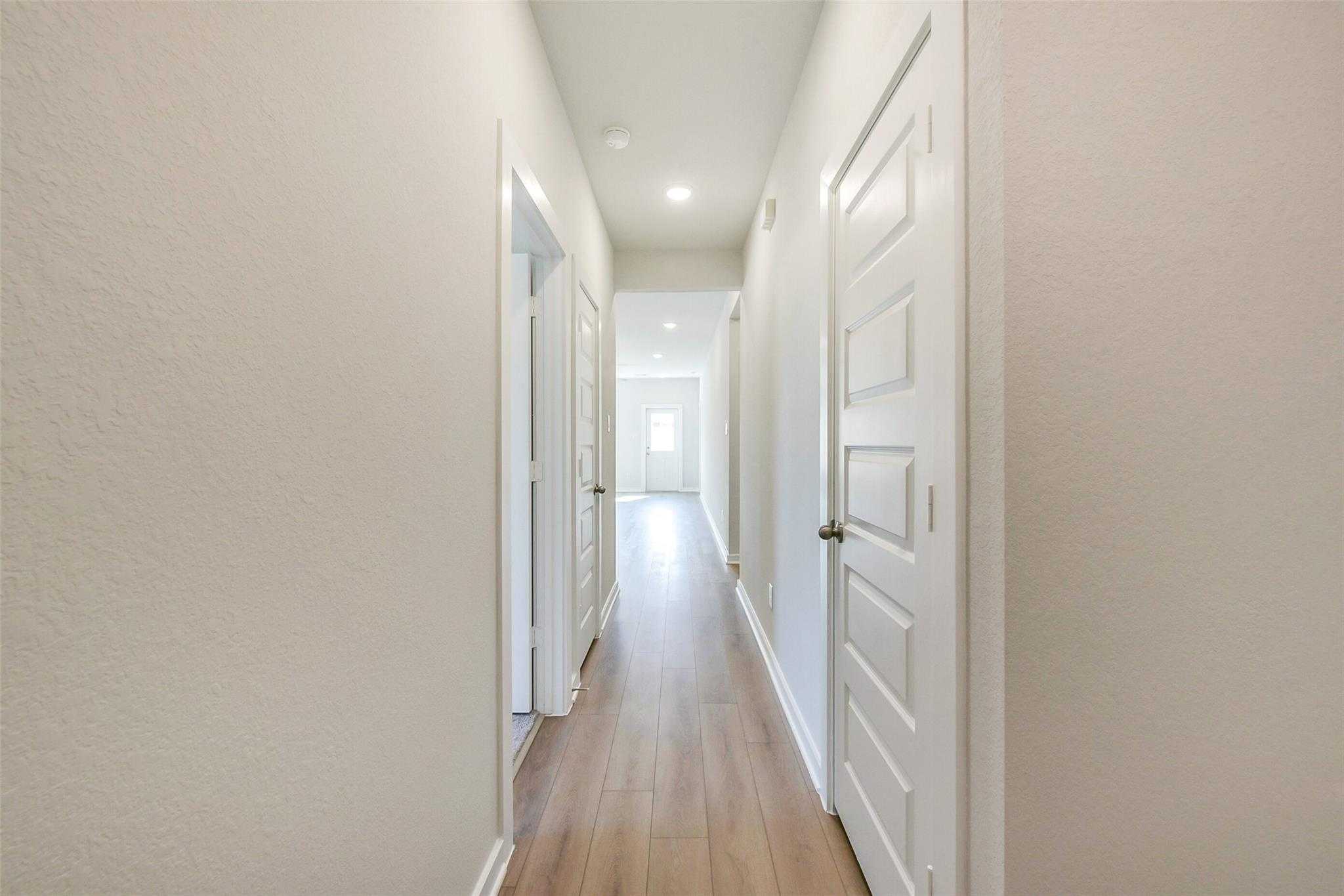 Bright hallway with light oak floors, white doors, and recessed lights in The Comal G 3-bedroom home, Dayton, Texas