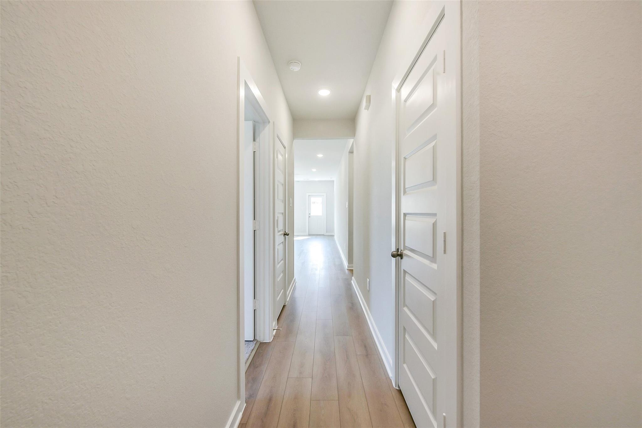 Bright hallway with white doors, recessed lights, and light wood floors in The Comal G 3-bedroom home, Dayton, Texas