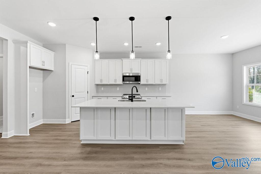 Modern white kitchen with spacious island, stainless appliances, and pendant lights in Davidson Homes The Montgomery B, Hartselle, AL
