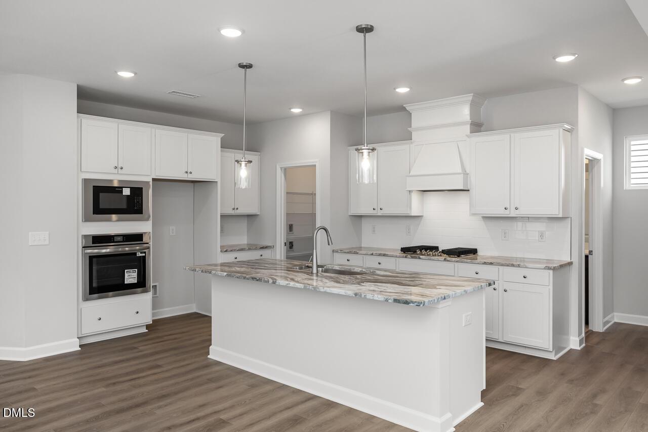 Modern kitchen with marble-style island, white cabinets, and stainless appliances in The Adalynn A, Gregory Village, NC.