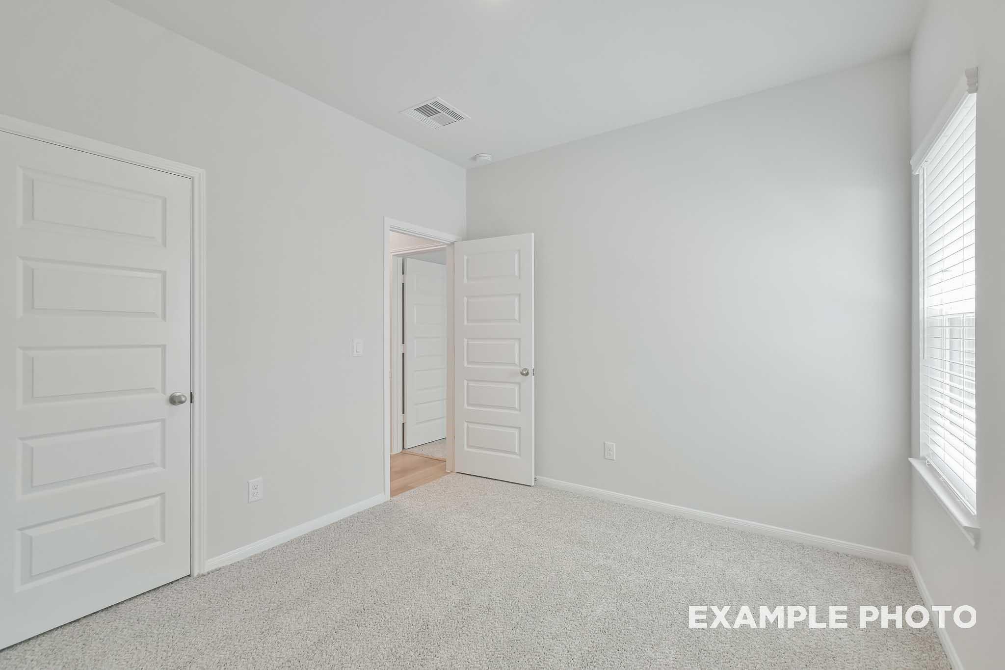 Bright secondary bedroom with white walls, neutral carpet, double doors, and window in Davidson Homes The Frio F, Conroe, Texas