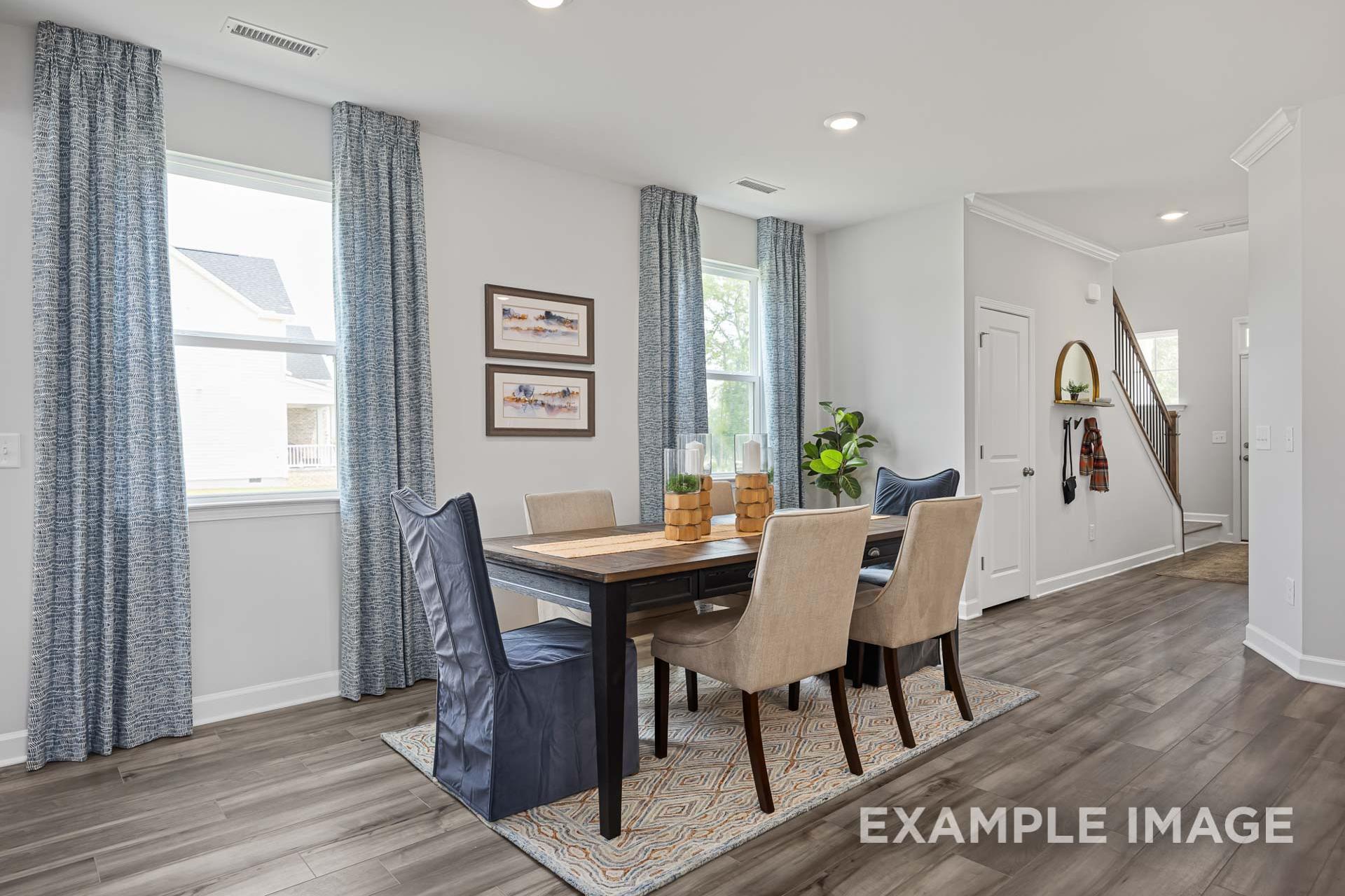 Spacious dining room in The Adalynn C with wooden table, upholstered chairs, blue curtains, nautical art, and open hallway
