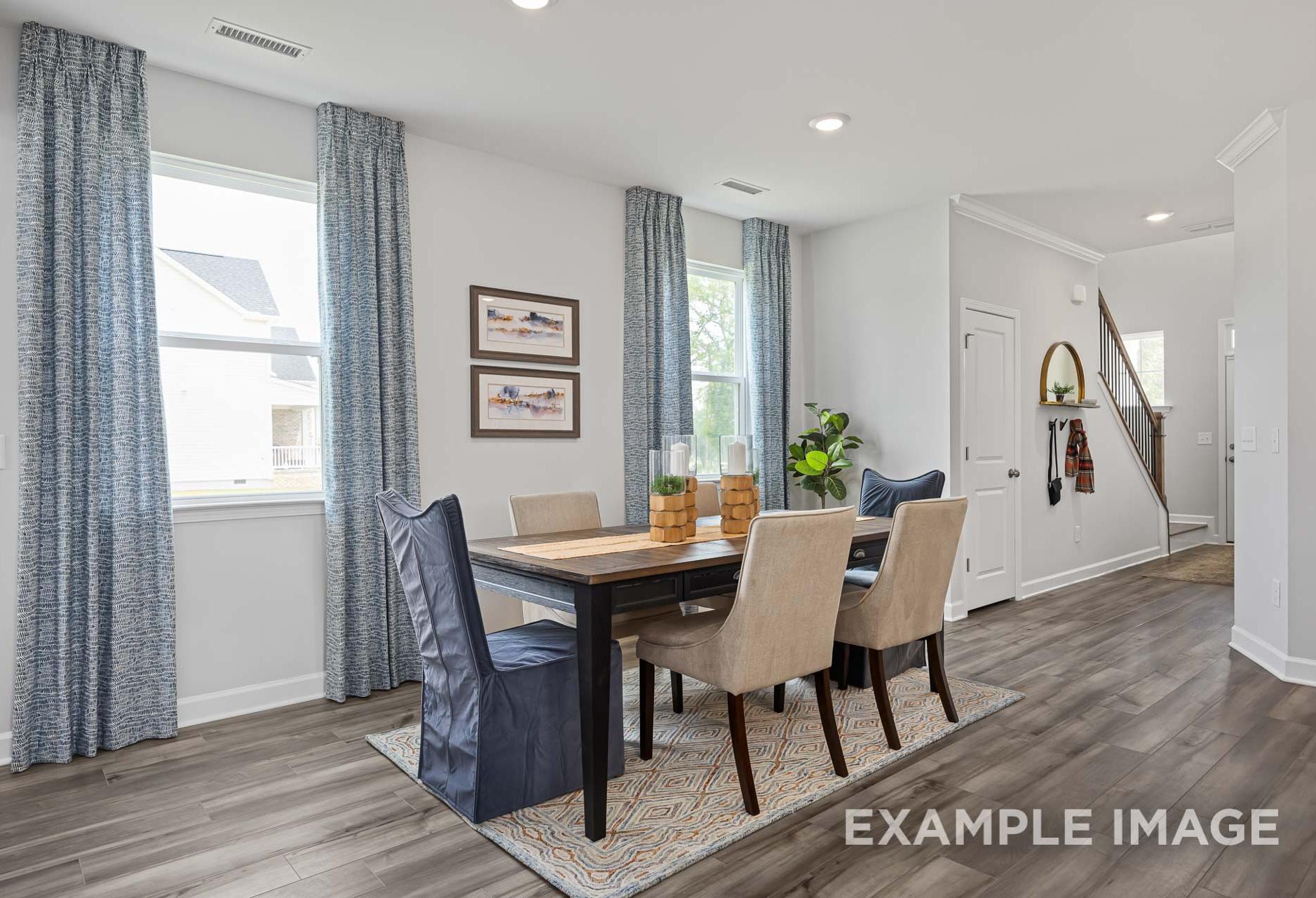 Spacious dining room in The Adalynn A home design featuring wooden table, upholstered chairs, blue curtains, and open hallway to stairs