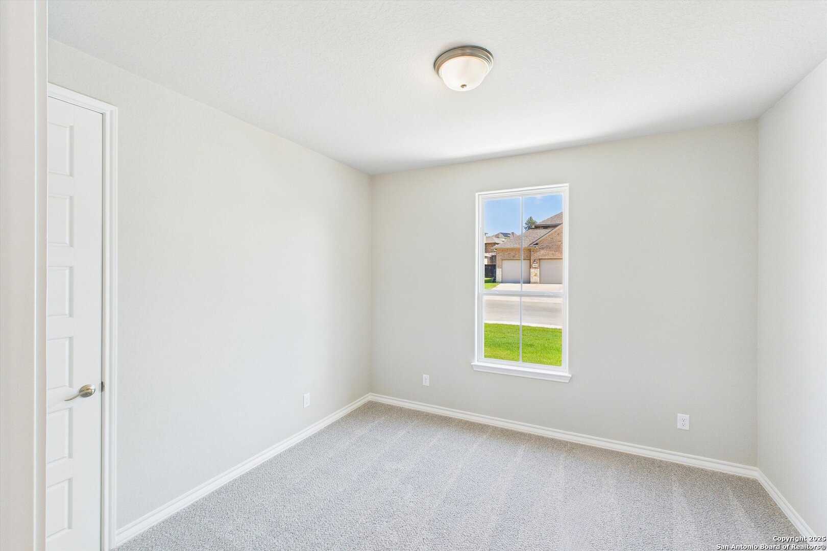 Bright secondary bedroom with neutral walls, beige carpet, and window overlooking green lawn in Davidson Homes The Jennings H, Ladera, San Antonio