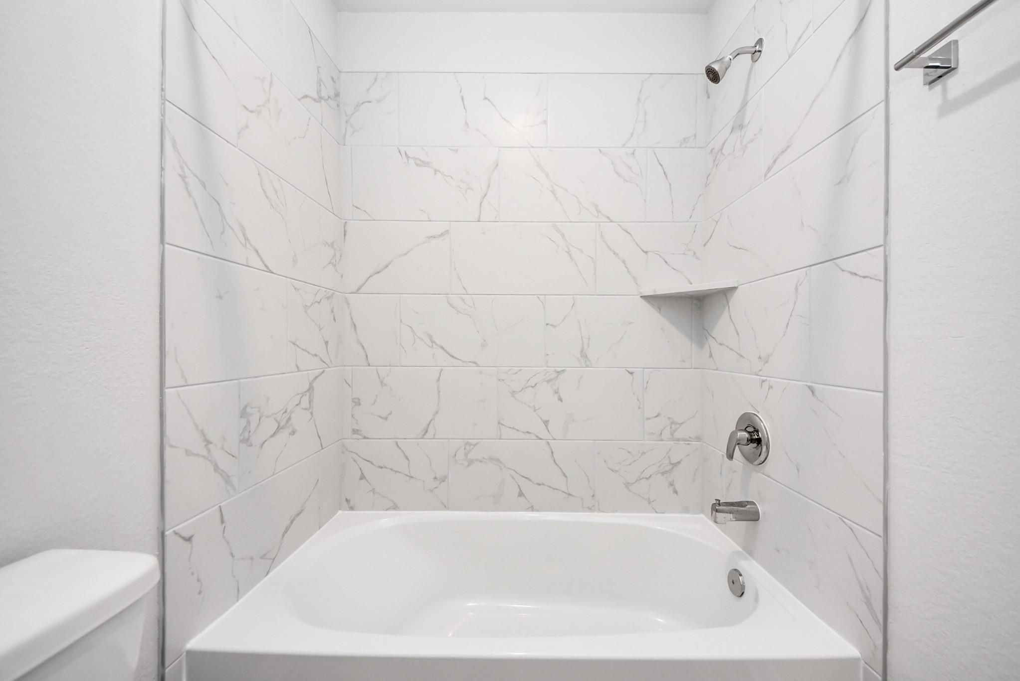Modern bathroom with white marble-look tile shower surround in The Sabine E floor plan at Windmill Estates, Magnolia.