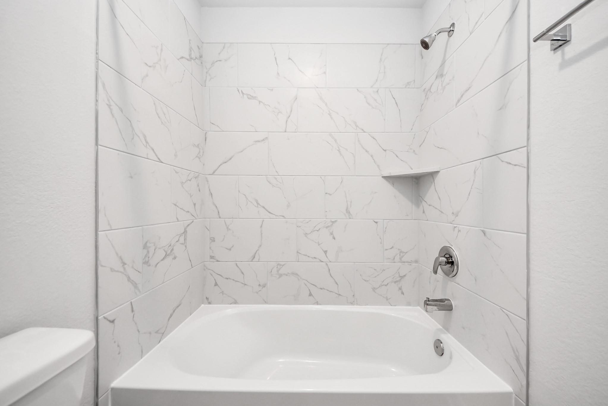 Modern bathroom with white marble-look tile shower surround in The Sabine E floor plan at Windmill Estates, Magnolia.