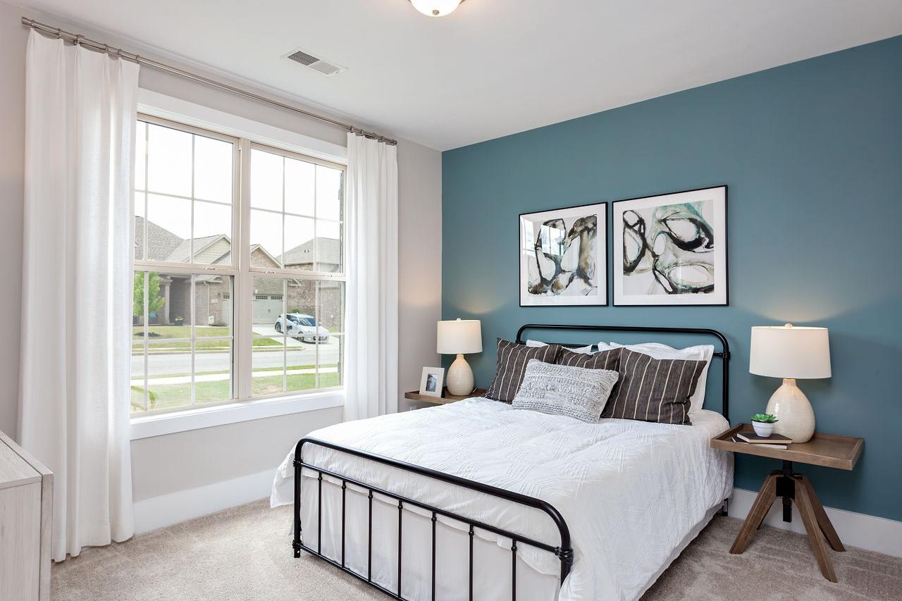 Cozy secondary bedroom in The Rockford with teal accent wall, black iron bed, white bedding, abstract art, and large window