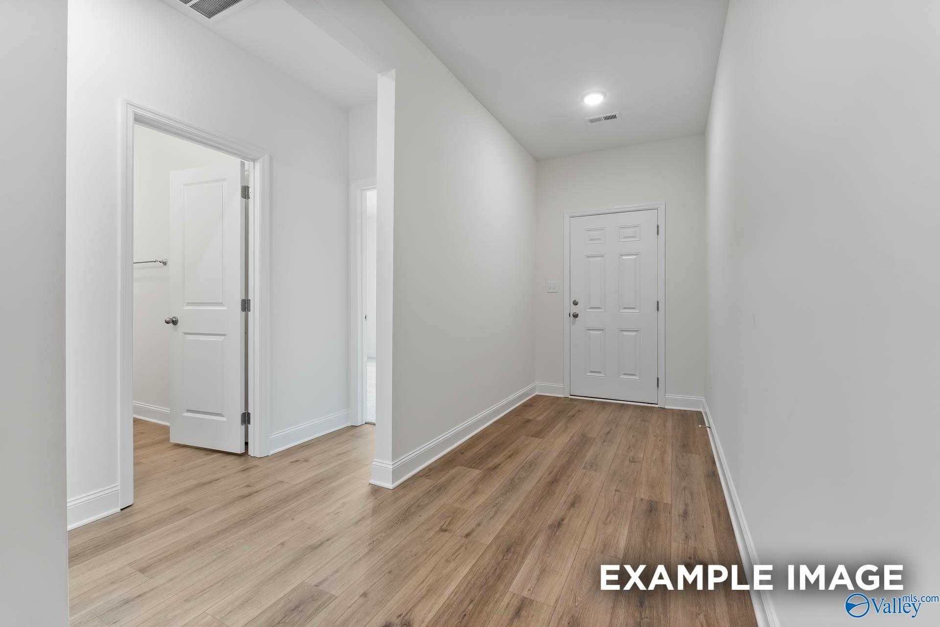 Bright hallway with light oak hardwood floors, white walls, and doors to bedrooms and bath in Davidson Homes The Daphne V, Athens, Alabama