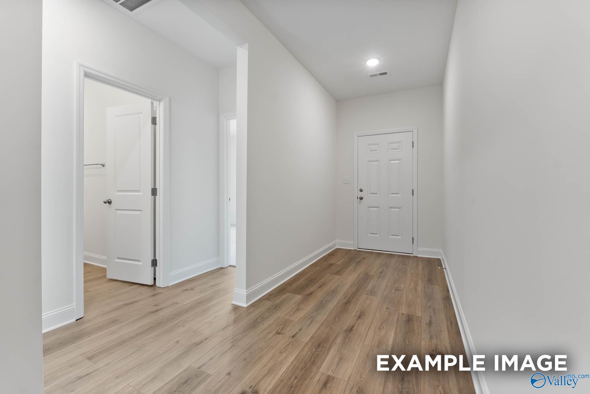 Bright hallway with light oak hardwood floors, white walls, and doors to bedrooms and bath in Davidson Homes The Daphne V, Athens, Alabama