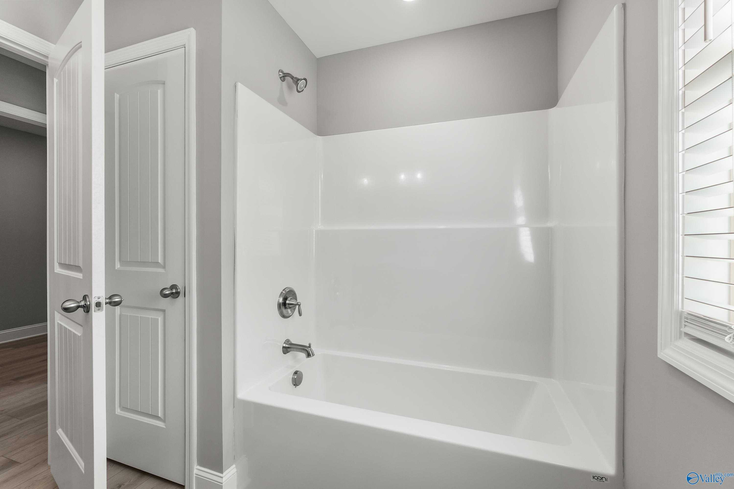 Contemporary bathroom with white tub-shower combo, gray walls, and window blinds in Davidson Homes The Everett B, Athens, Alabama