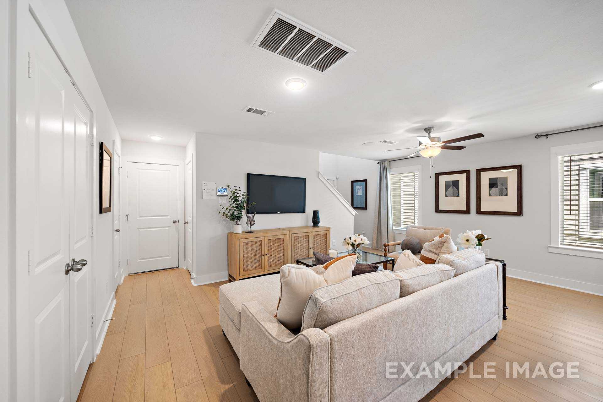 Spacious living room in The Rose B by Davidson Homes featuring beige sectional sofa, wall-mounted TV, hardwood floors, and large windows in Cypress, Texas