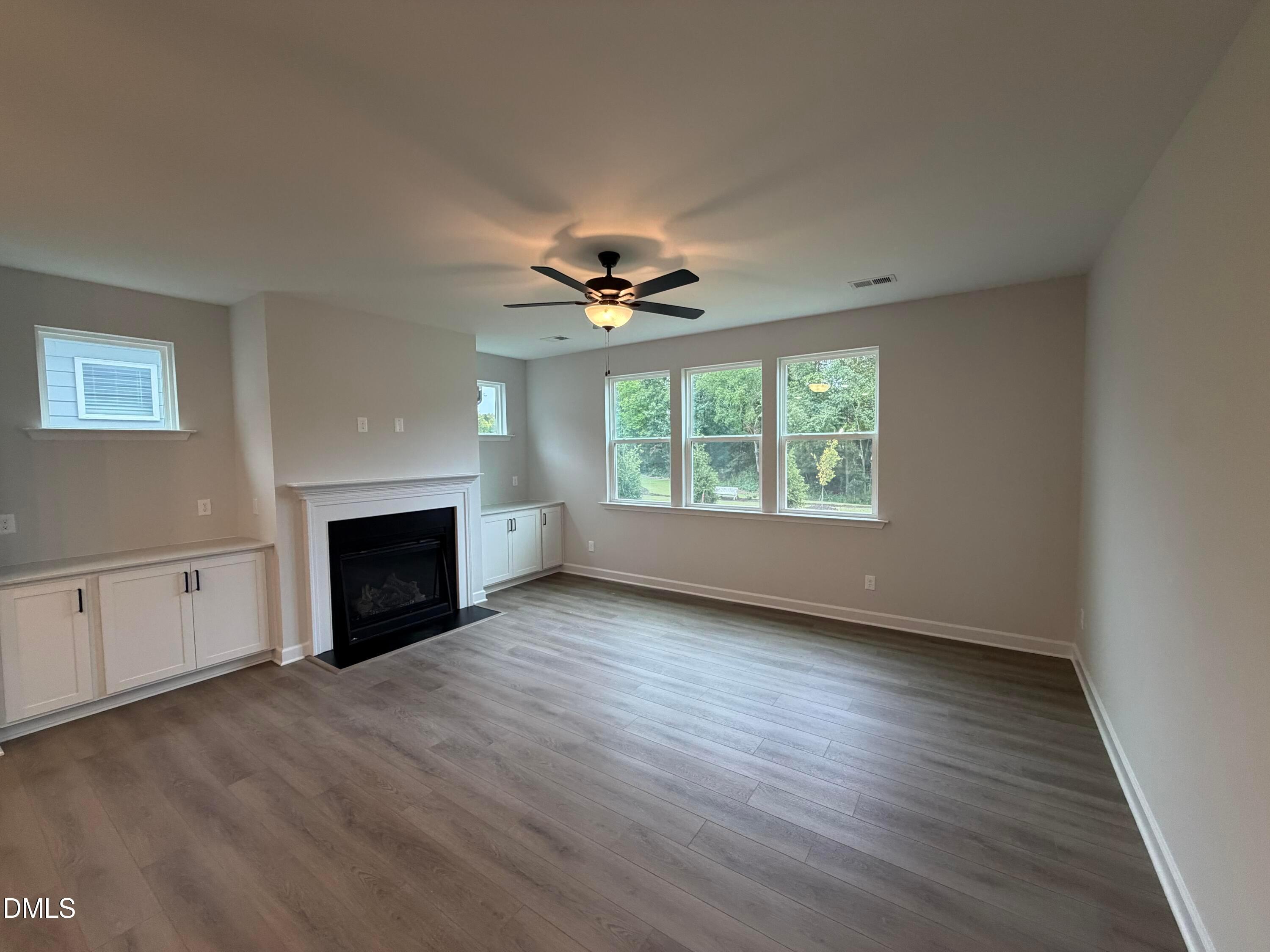 Great room with gas fireplace, white built-ins, luxury vinyl plank flooring, and ceiling fan in Davidson Homes The Preston C, Wendell NC