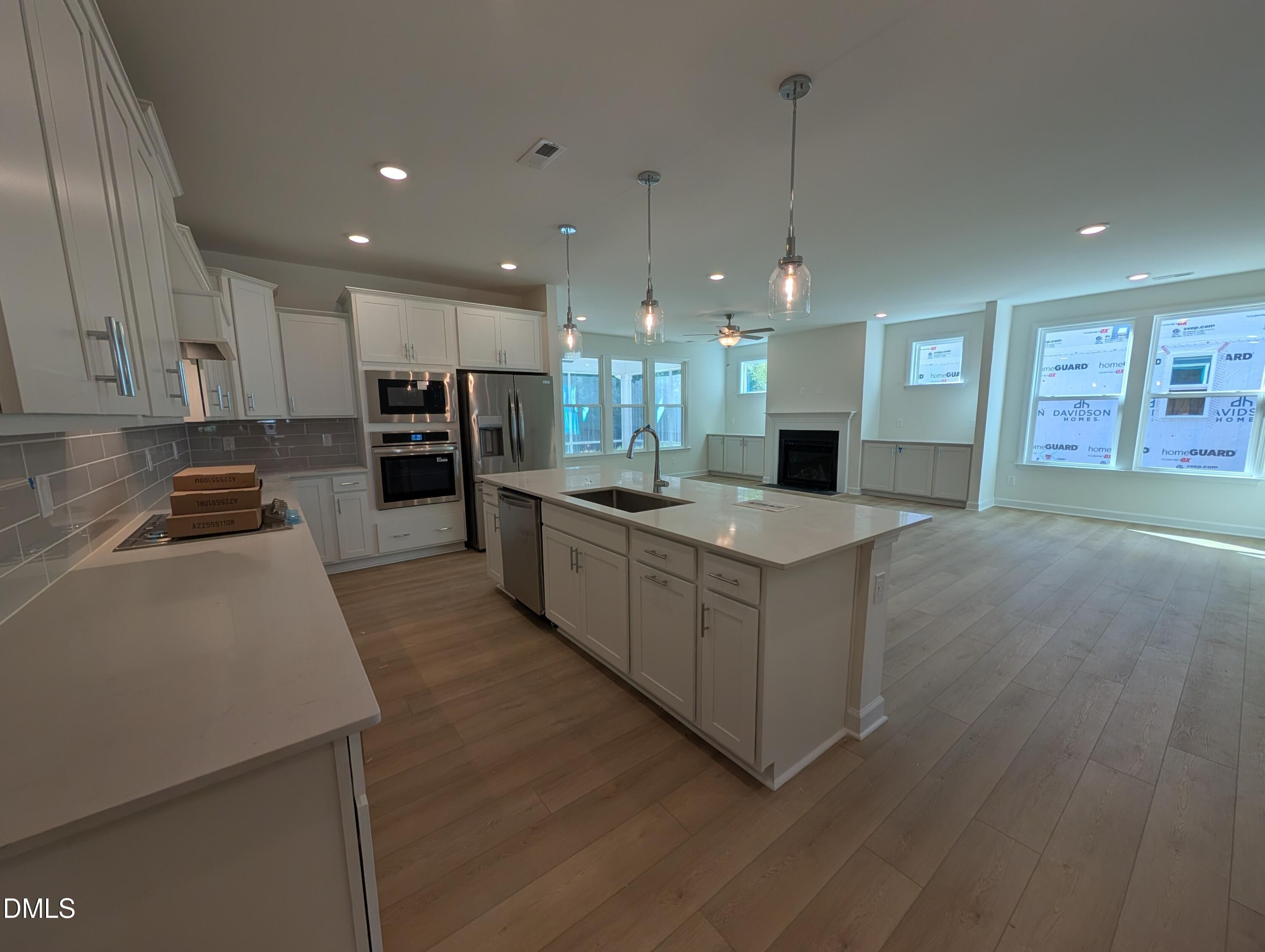 Open-concept kitchen with white cabinetry, large island, stainless appliances, and fireplace in Davidson Homes Magnolia A, Wendell Ridge NC