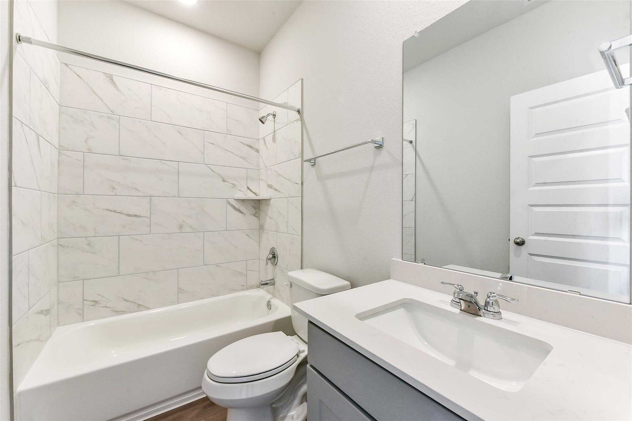 Modern guest bathroom featuring white subway tile shower-tub combo, gray vanity, and mirror in Davidson Homes The Laguna C 3-car garage, Rosharon, Texas