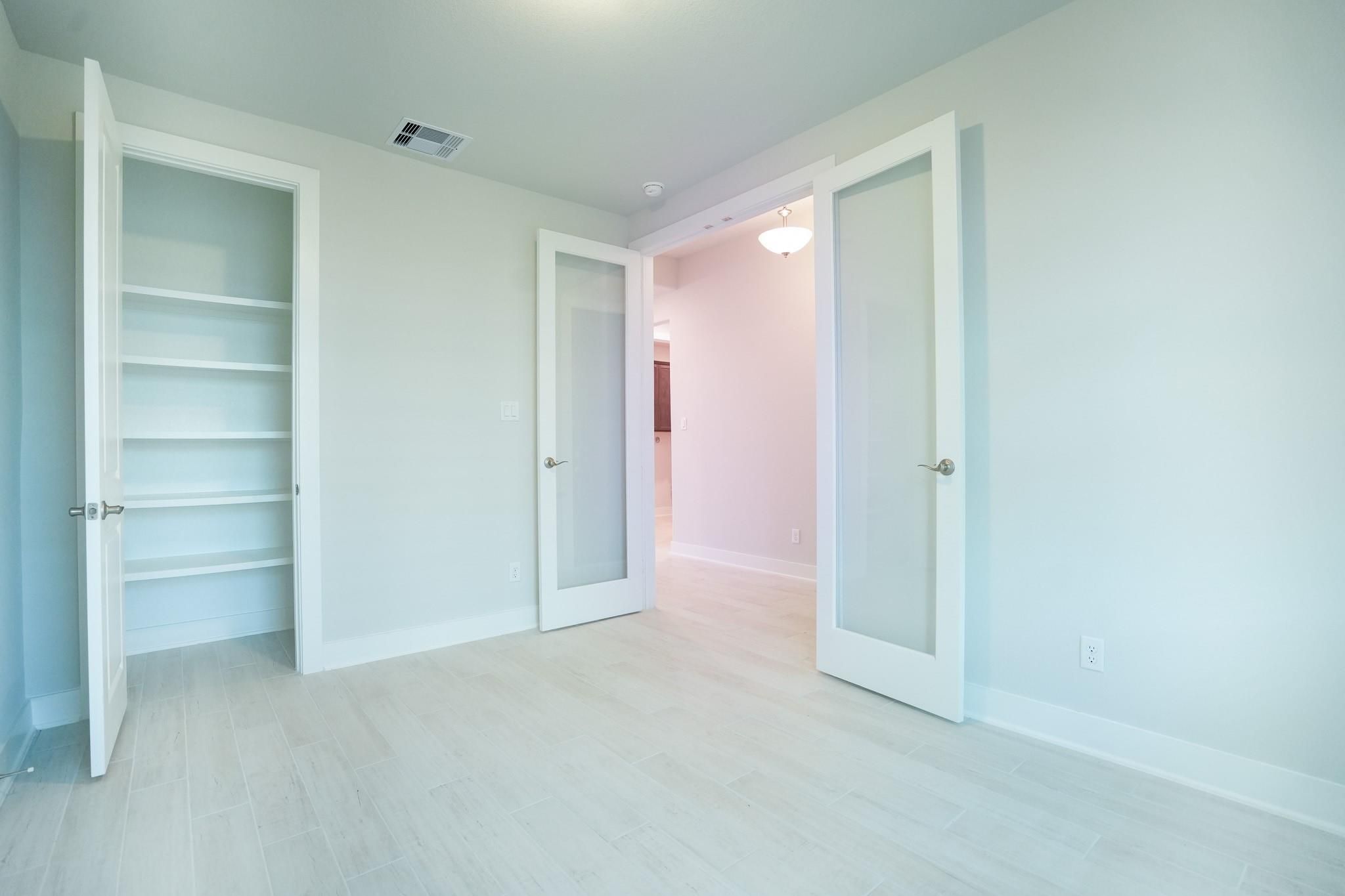 Spacious bedroom with open walk-in closet shelves and glass French doors in Davidson Homes The Edward C, Lago Mar, Texas City