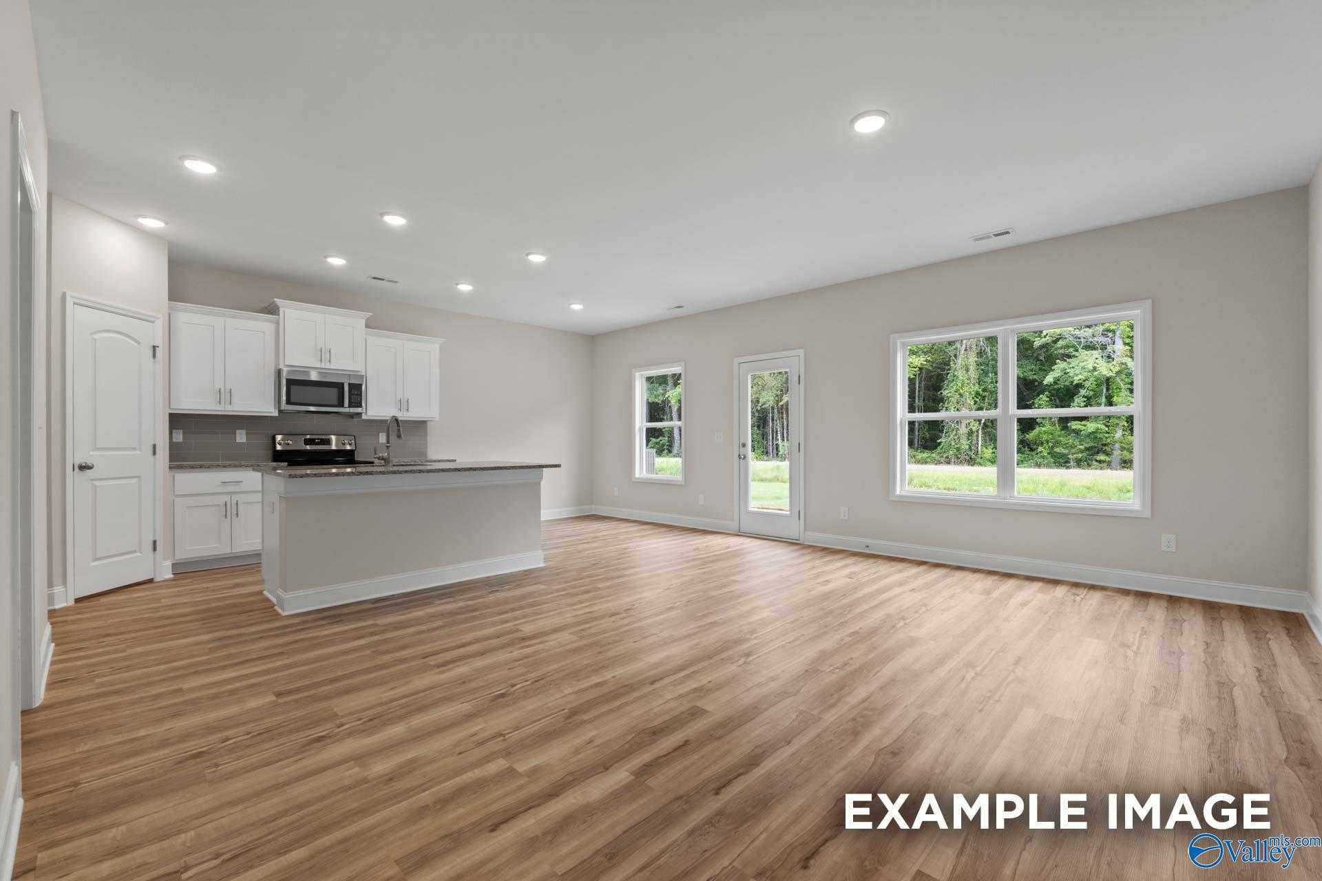 Open-concept kitchen and living space with wood floors, white cabinets, and large windows to backyard in Davidson Homes The Butler, New Market, Alabama
