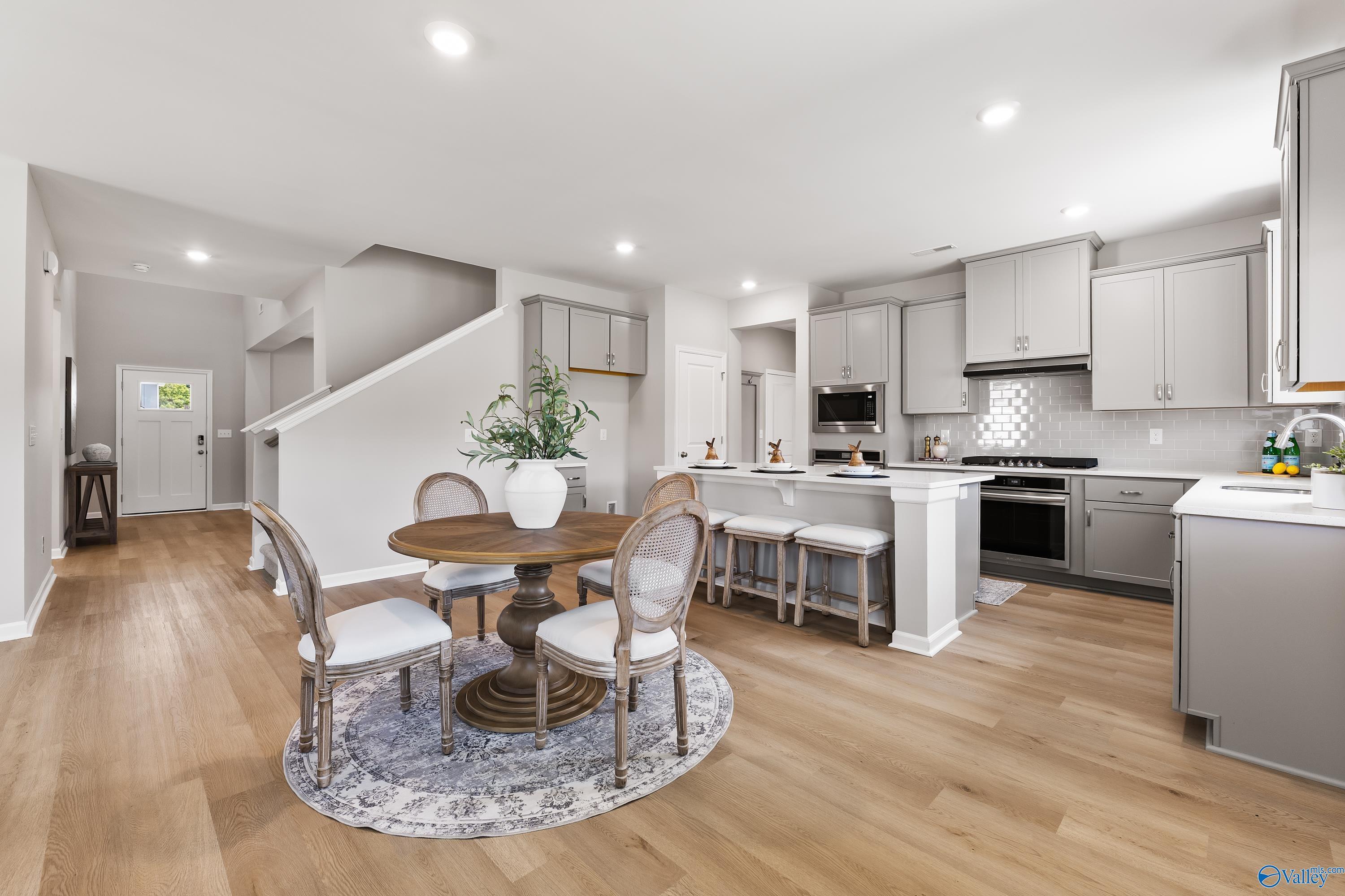 Elegant open dining area with round wood table, white chairs, and adjacent gray kitchen island in Davidson Homes The Charm, Huntsville AL
