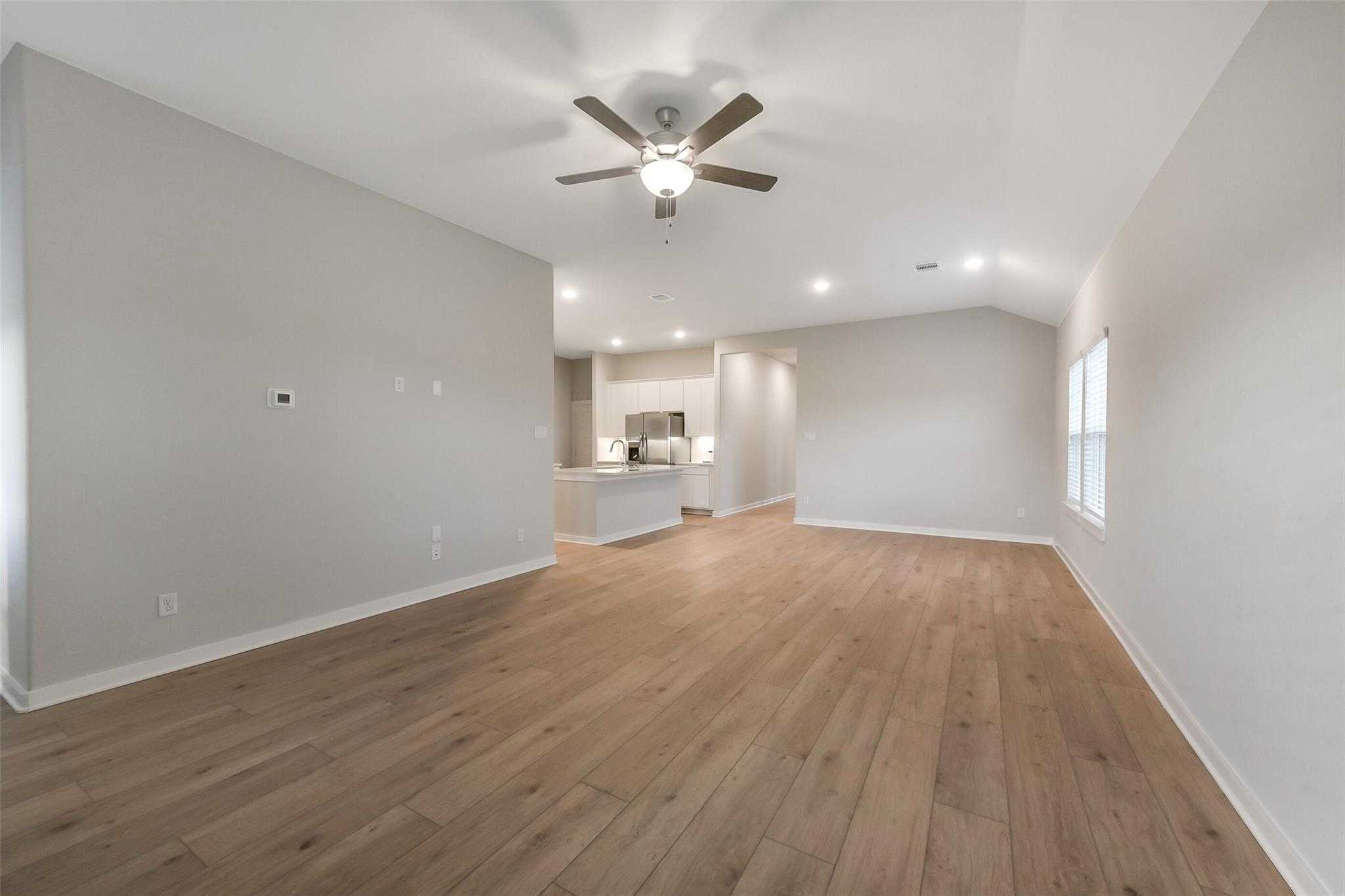 Open-concept living area with hardwood floors, ceiling fan, and kitchen view in Davidson Homes The Laguna B, Sunterra, Katy, Texas