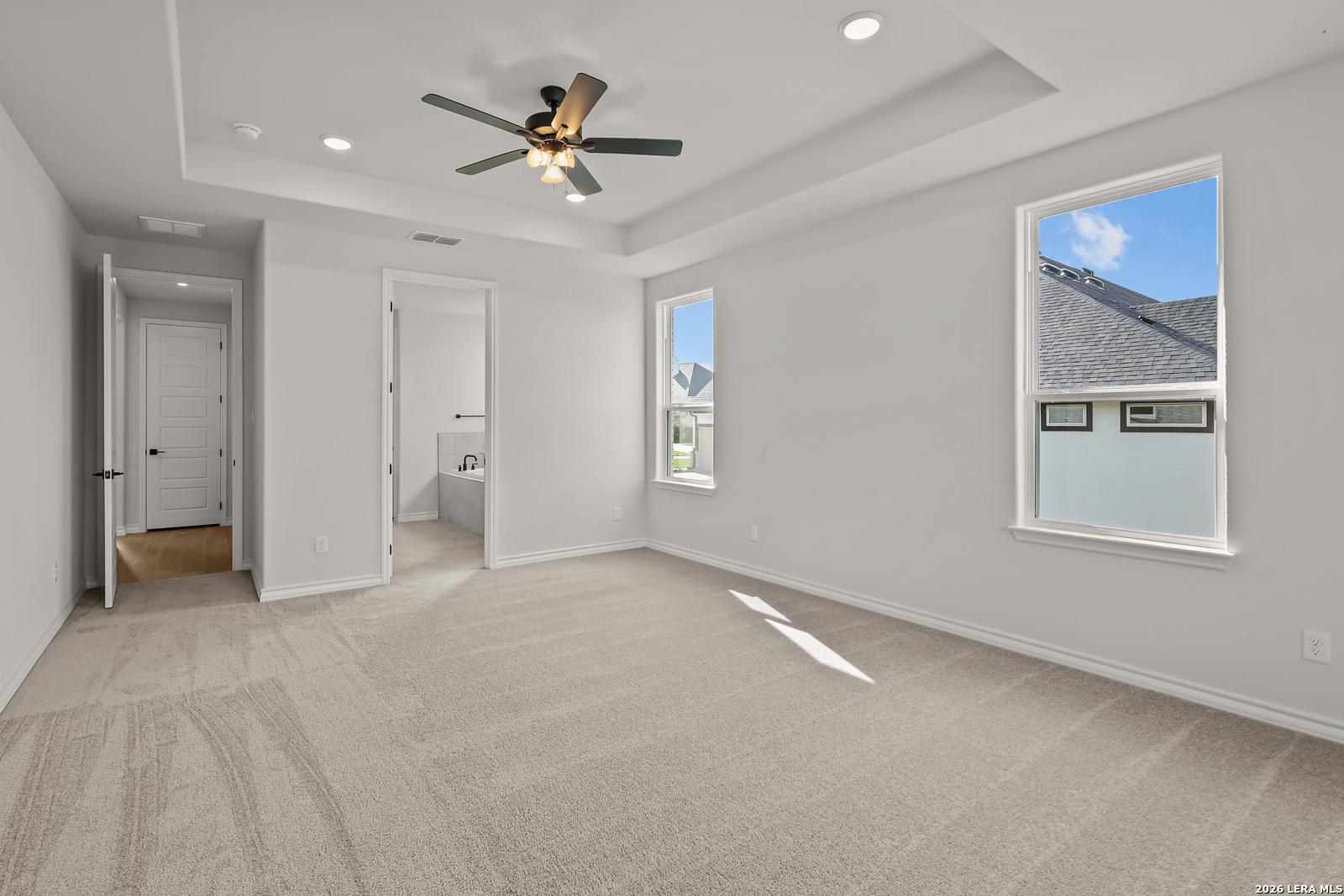 Spacious primary bedroom with tray ceiling, ceiling fan, and carpet flooring in Davidson Homes The Oxford F, Castroville, Texas