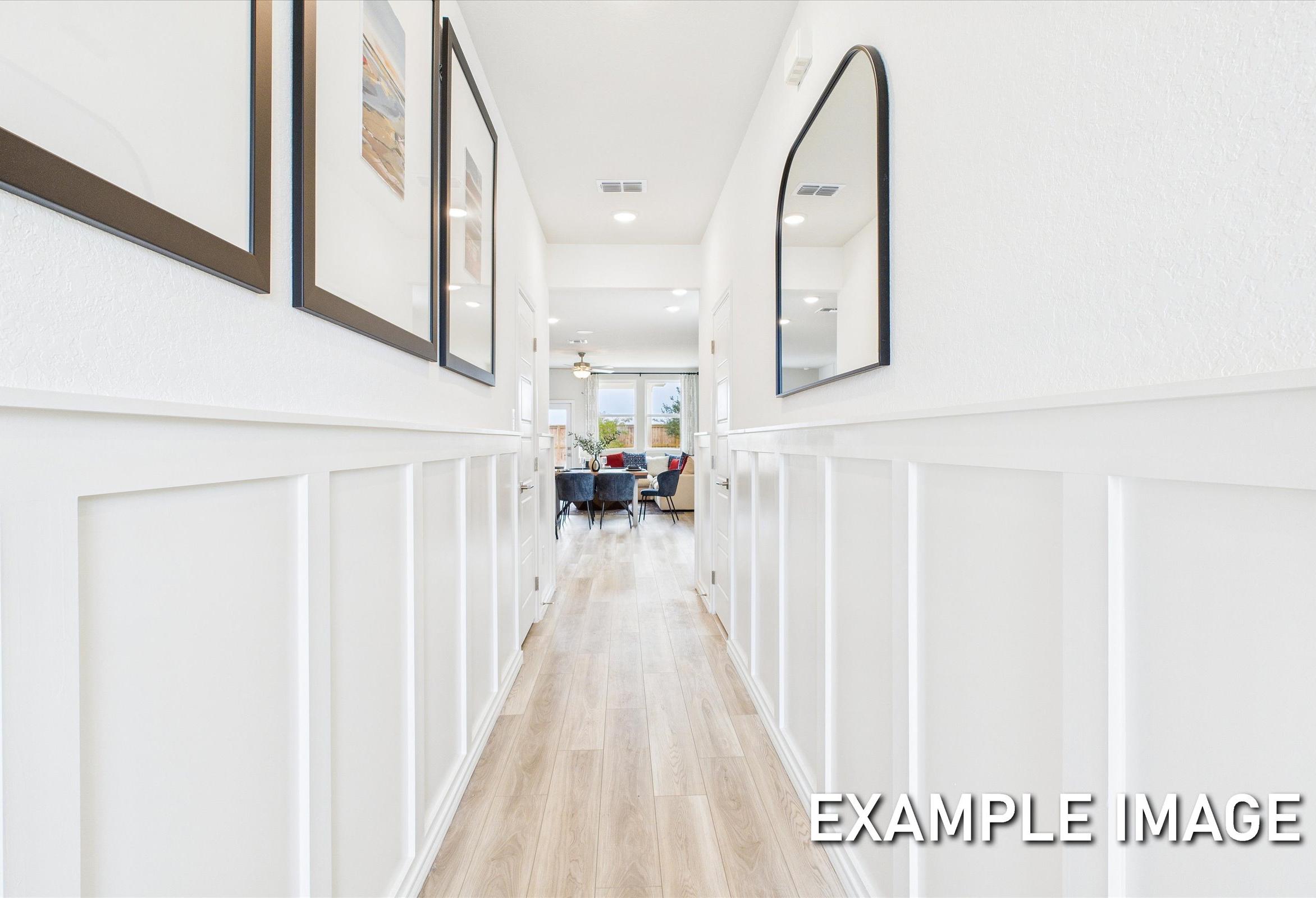 Spacious hallway in The Brazos A home featuring white wainscoting, framed art, mirrors, hardwood floors, and open living area