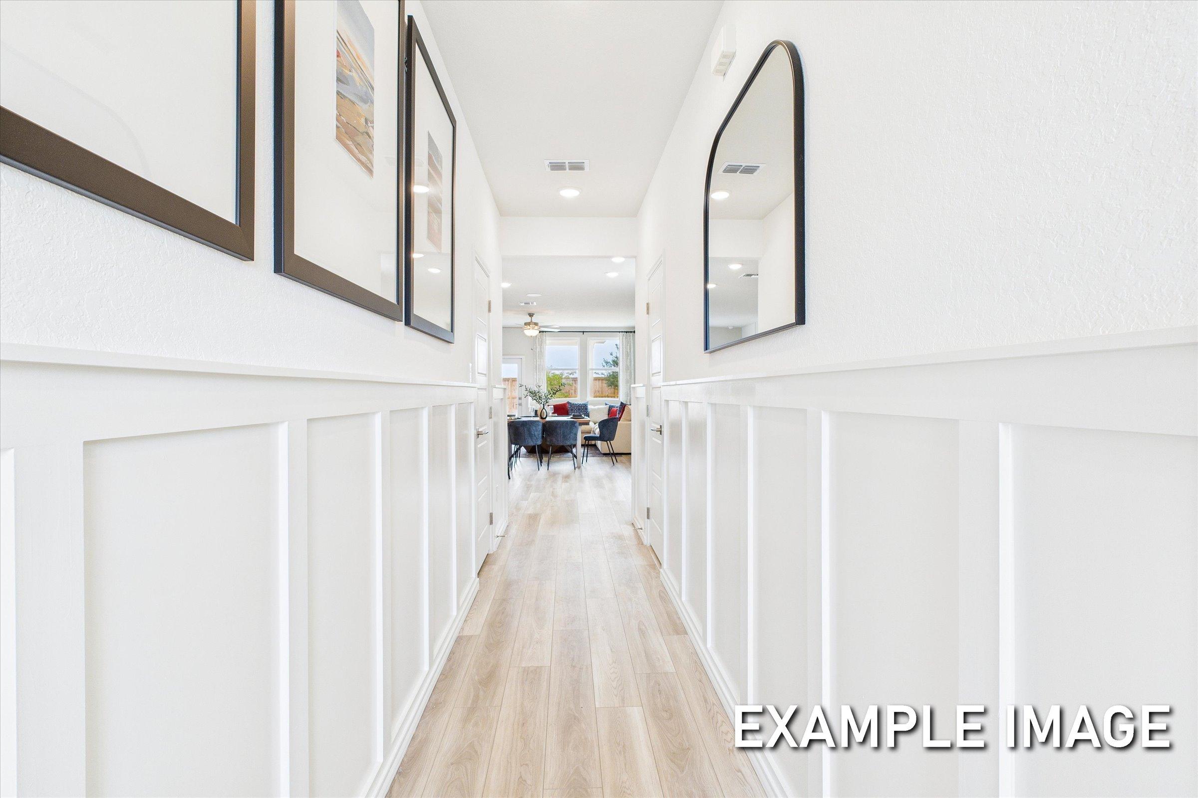 Spacious hallway in The Brazos home featuring white wainscoting, light oak floors, framed art, and round mirror