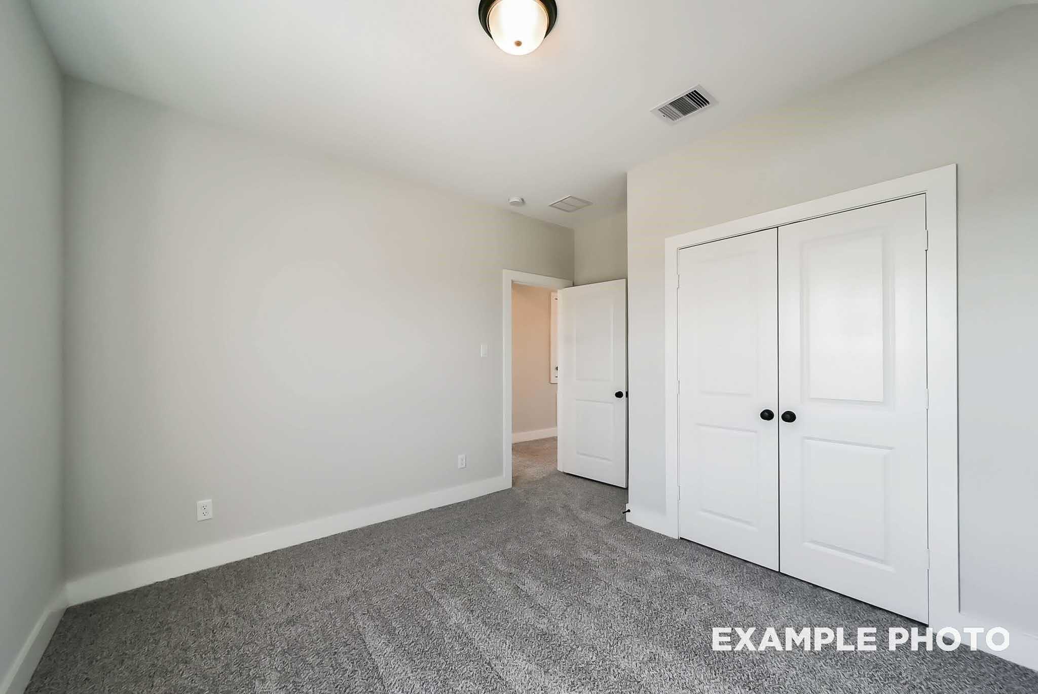 Bright bedroom with gray carpet, light gray walls, ceiling fan, and white double closet doors in Davidson Homes The Philip C, Rosharon, Texas