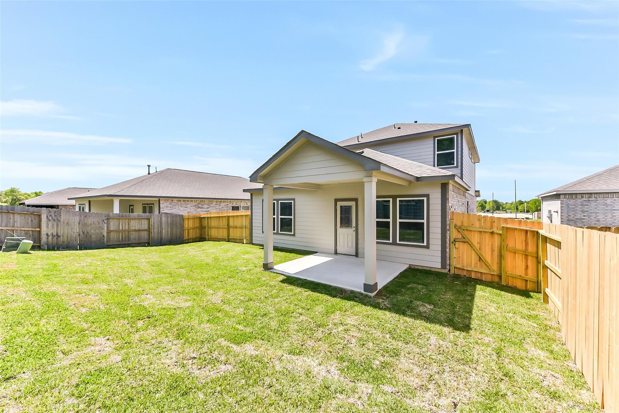 Covered back patio with wooden columns, lush green lawn, and privacy fence in Davidson Homes The Brazos E, Windmill Estates, Magnolia, Texas