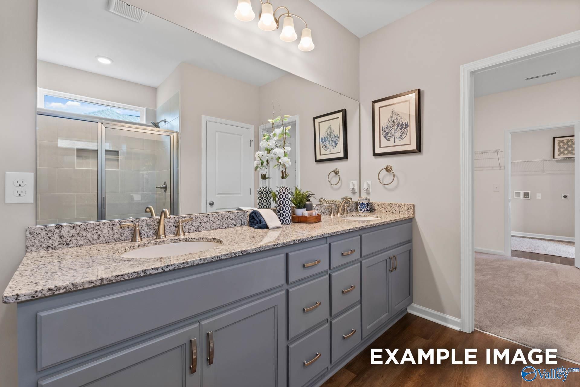 Elegant master bathroom featuring double granite vanity, gray cabinets, large mirror, and glass shower in The Arcadia M, Owens Cross Roads, Alabama