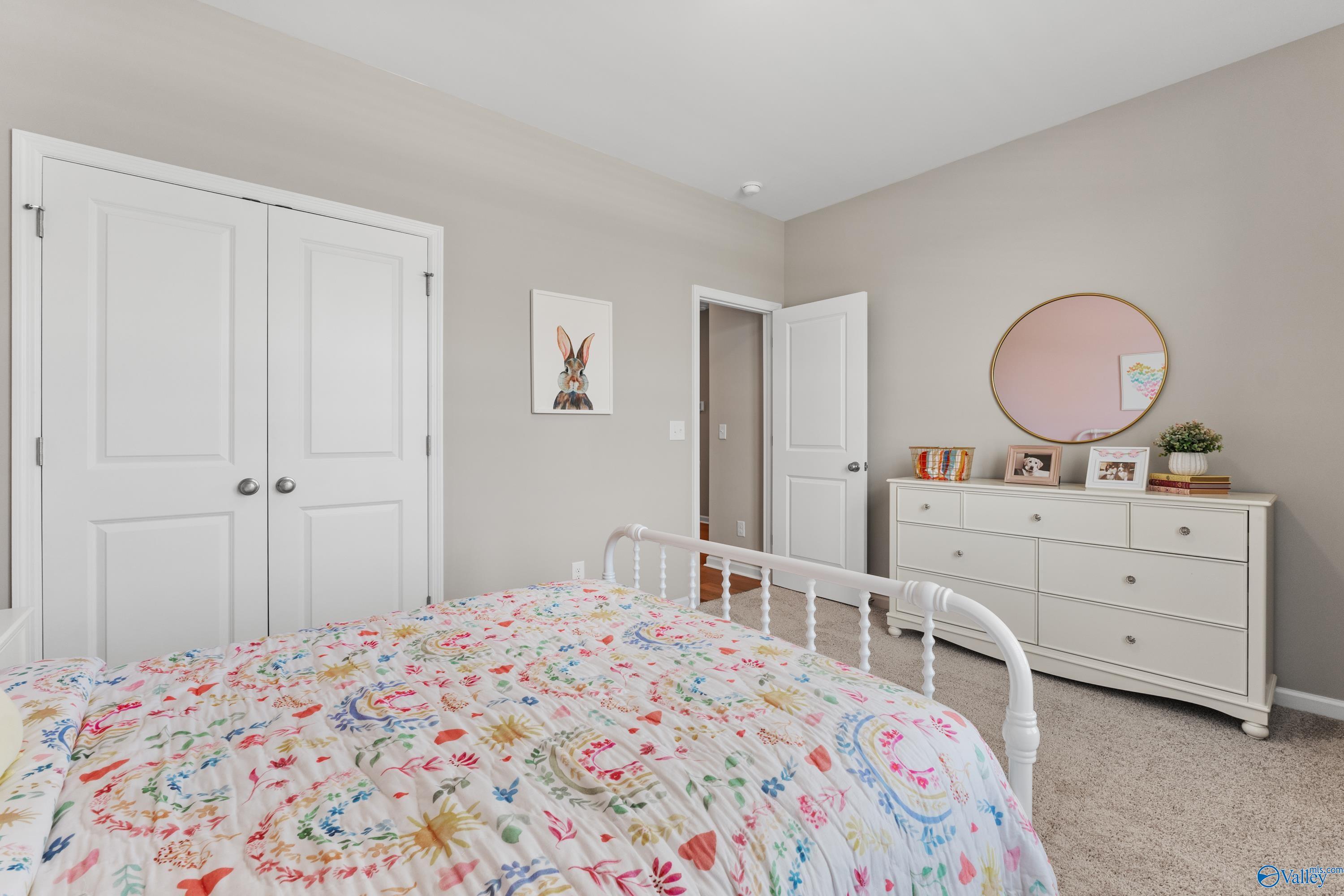 Charming bedroom with floral bedspread on white metal frame, dresser, pink mirror, and wall art in Davidson Homes The Sanctuary, Athens, Alabama