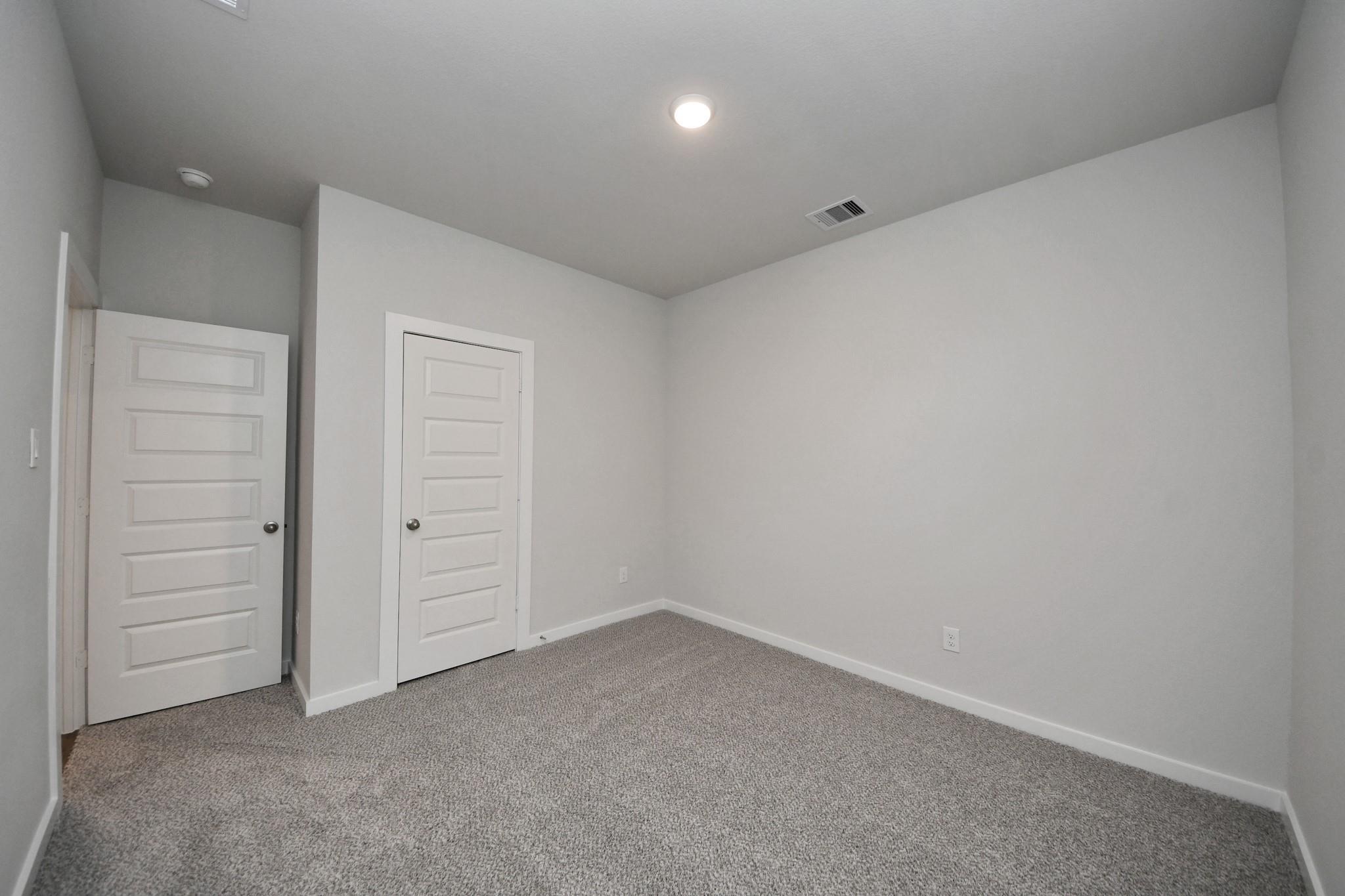 Empty bedroom with gray carpet, neutral walls, and white doors in Davidson Homes The Frio F plan at Robins Landing, Houston, Texas