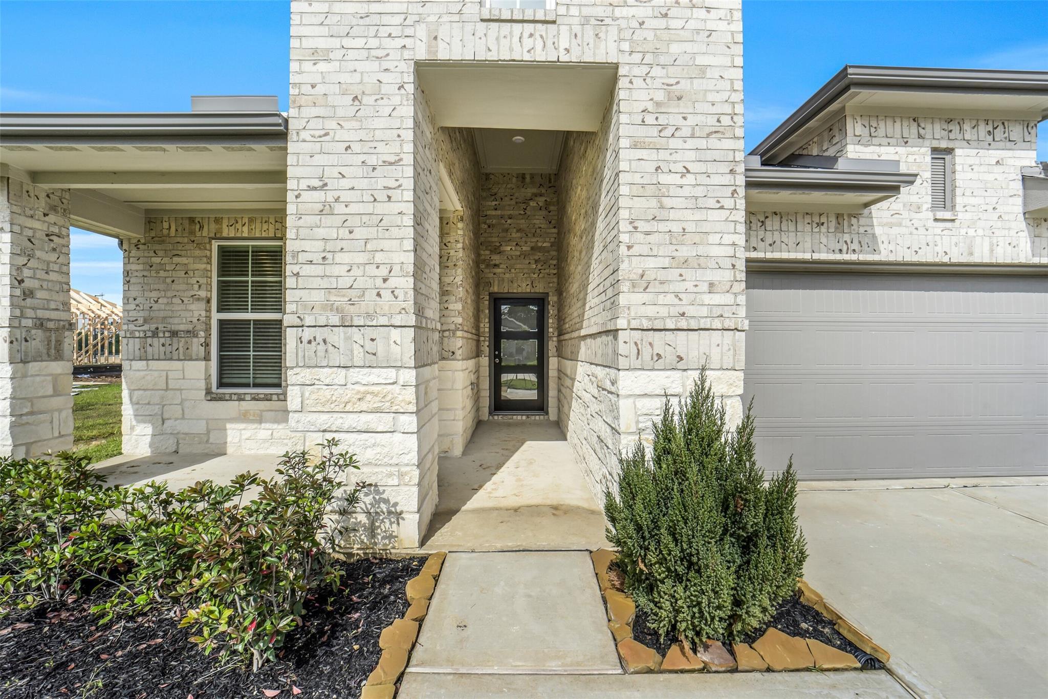 Modern white brick single-story home with covered entry porch, two-car garage, and landscaped front yard in Windmill Estates, Magnolia, Texas