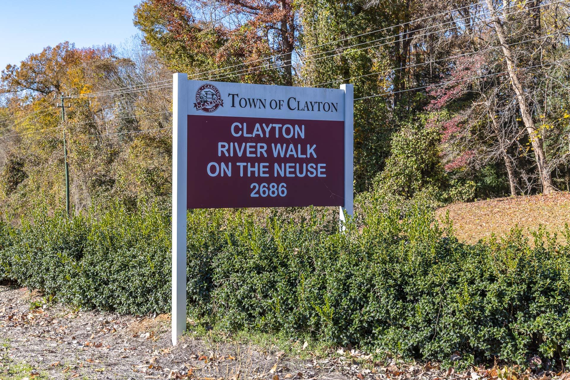 Clayton River Walk sign on the Neuse in Clayton NC with town emblem, autumn trees, and shrubs at 26866