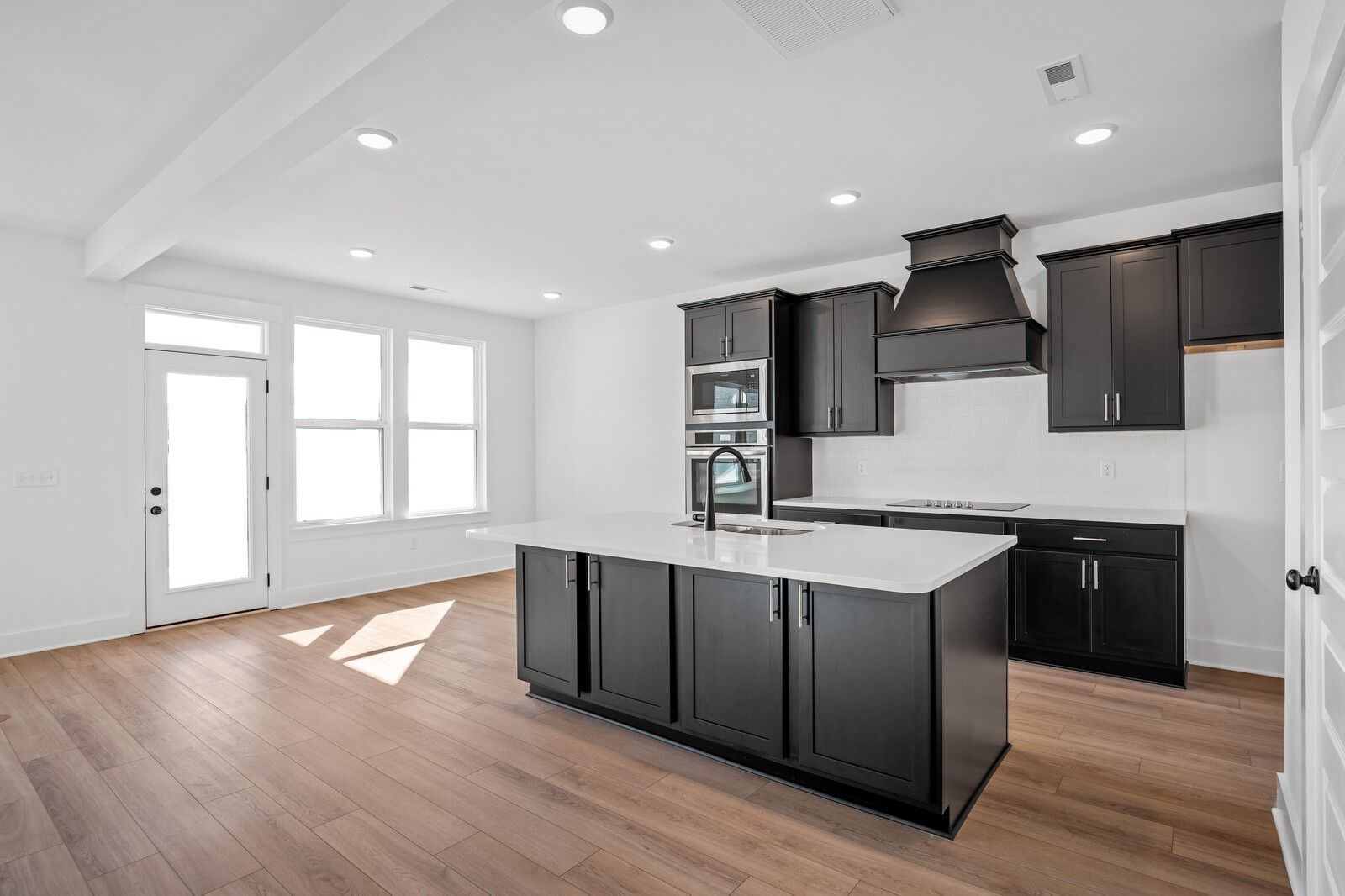 Modern kitchen with dark cabinets, white quartz island, stainless appliances, and large windows in The Willow C by Davidson Homes, Gallatin, TN