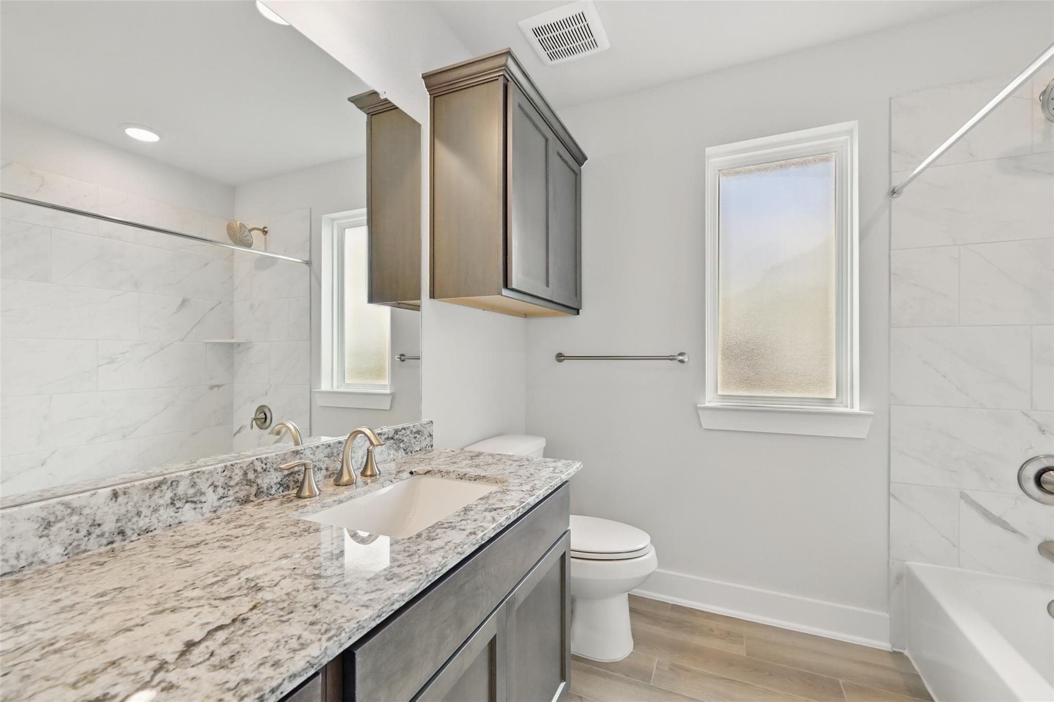 Modern bathroom with white subway tile, gray shaker cabinets, quartz vanity, soaking tub, and large window in Davidson Homes The Philip A, Lago Mar, Texas City