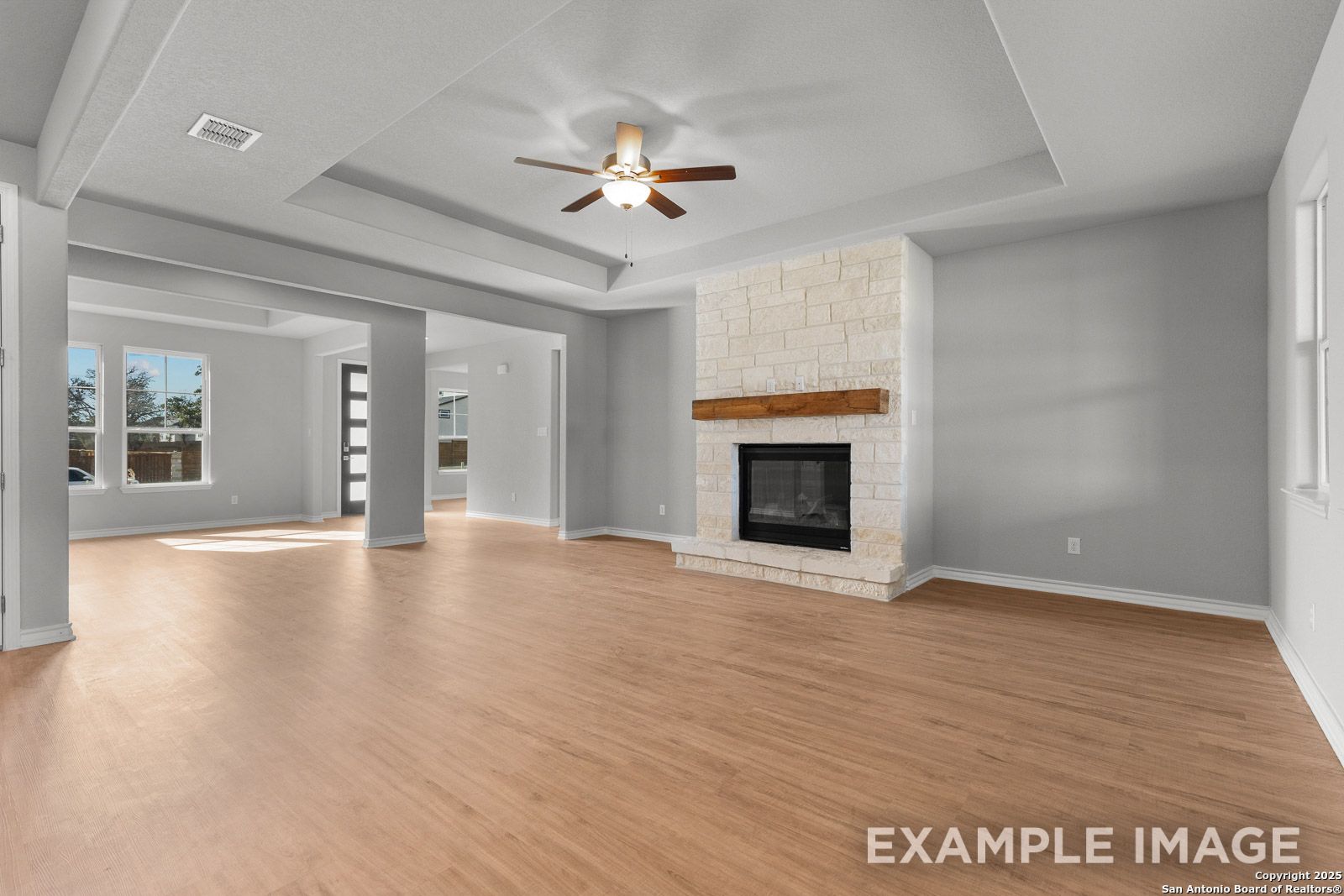 Spacious living room in The Oxford H featuring a stone fireplace, tray ceiling, and open-concept design in Castroville, TX.