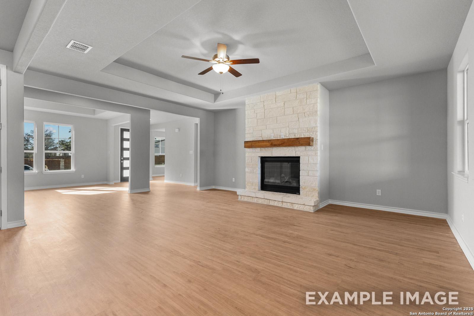 Spacious living room in The Oxford H featuring a stone fireplace, tray ceiling, and open-concept design in Castroville, TX.