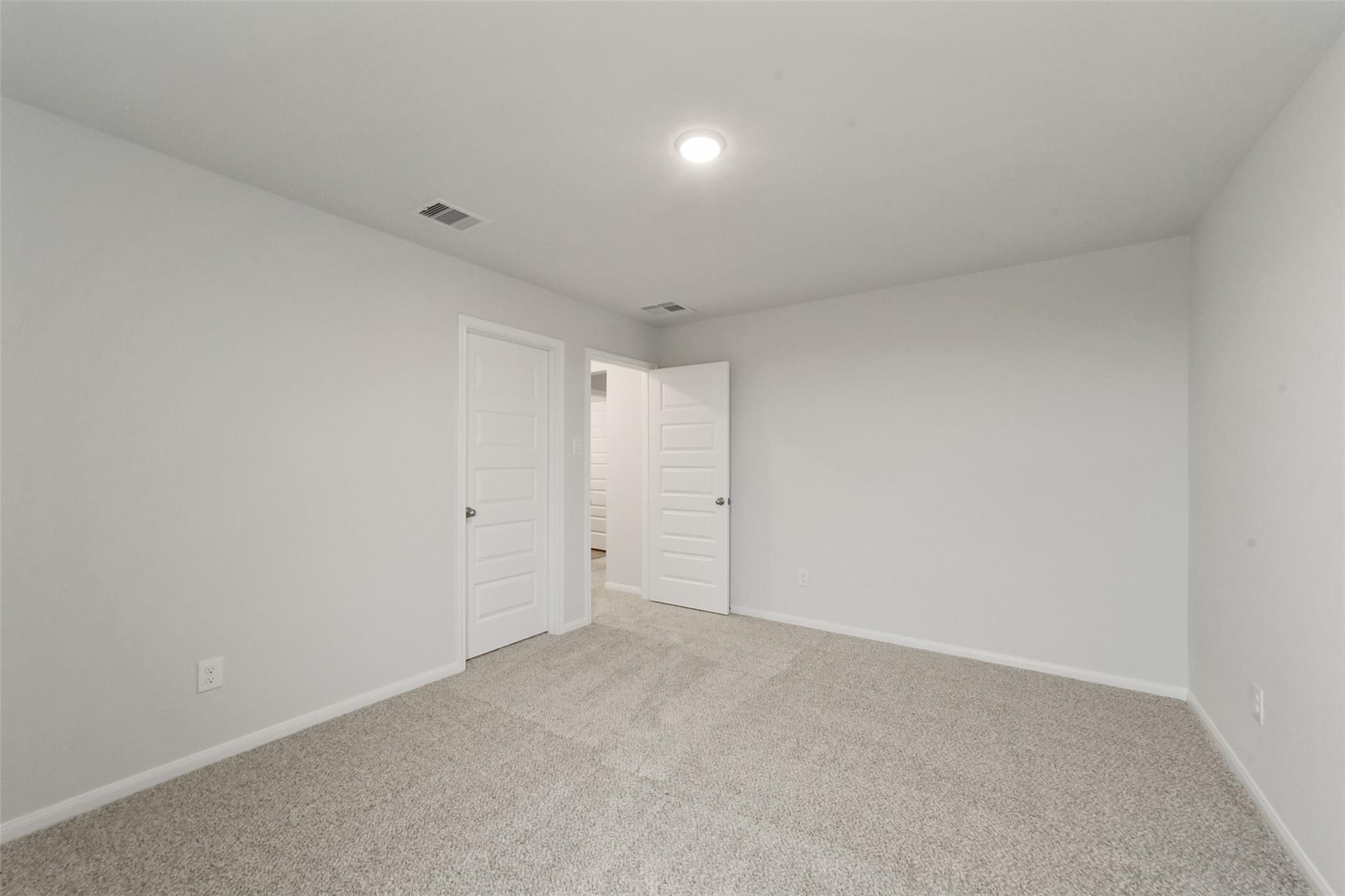 Empty bedroom with neutral walls, carpet flooring, and adjacent bathroom in Davidson Homes San Marcos E, Beasley, Texas