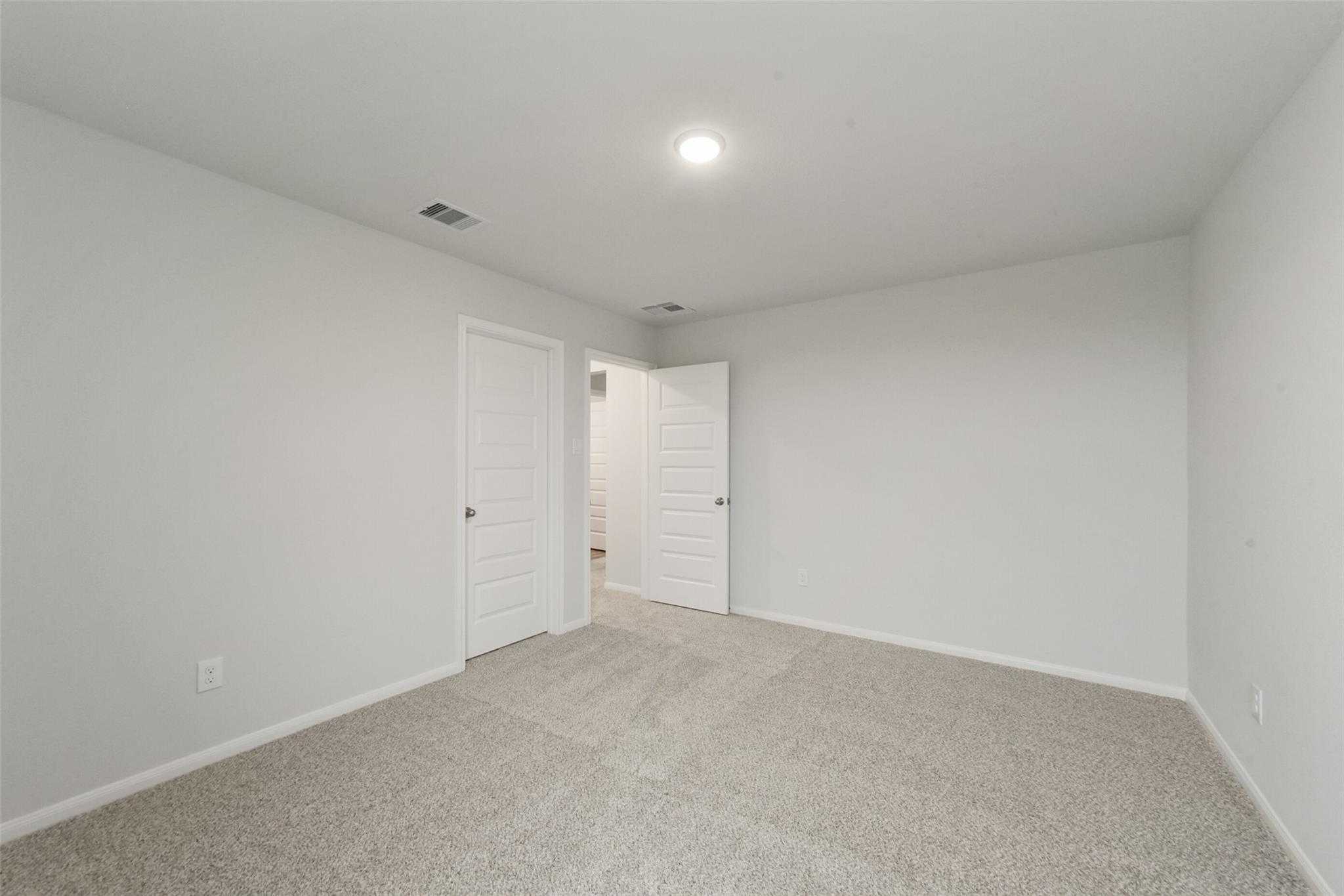 Empty bedroom with neutral walls, carpet flooring, and adjacent bathroom in Davidson Homes San Marcos E, Beasley, Texas