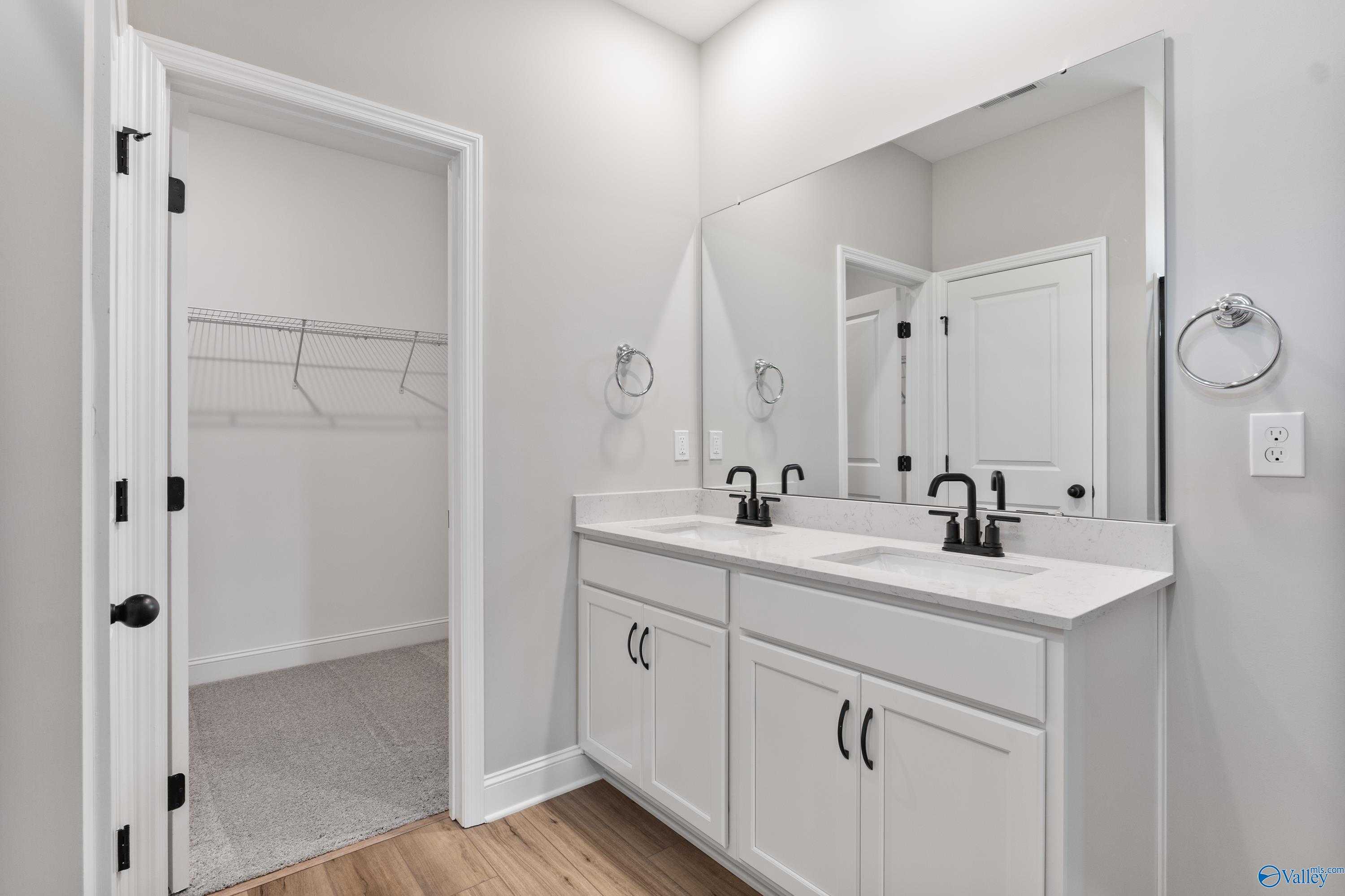Modern master bathroom featuring double vanity sinks, large framed mirror, and open walk-in closet in Davidson Homes The Franklin B, Hazel Green, Alabama