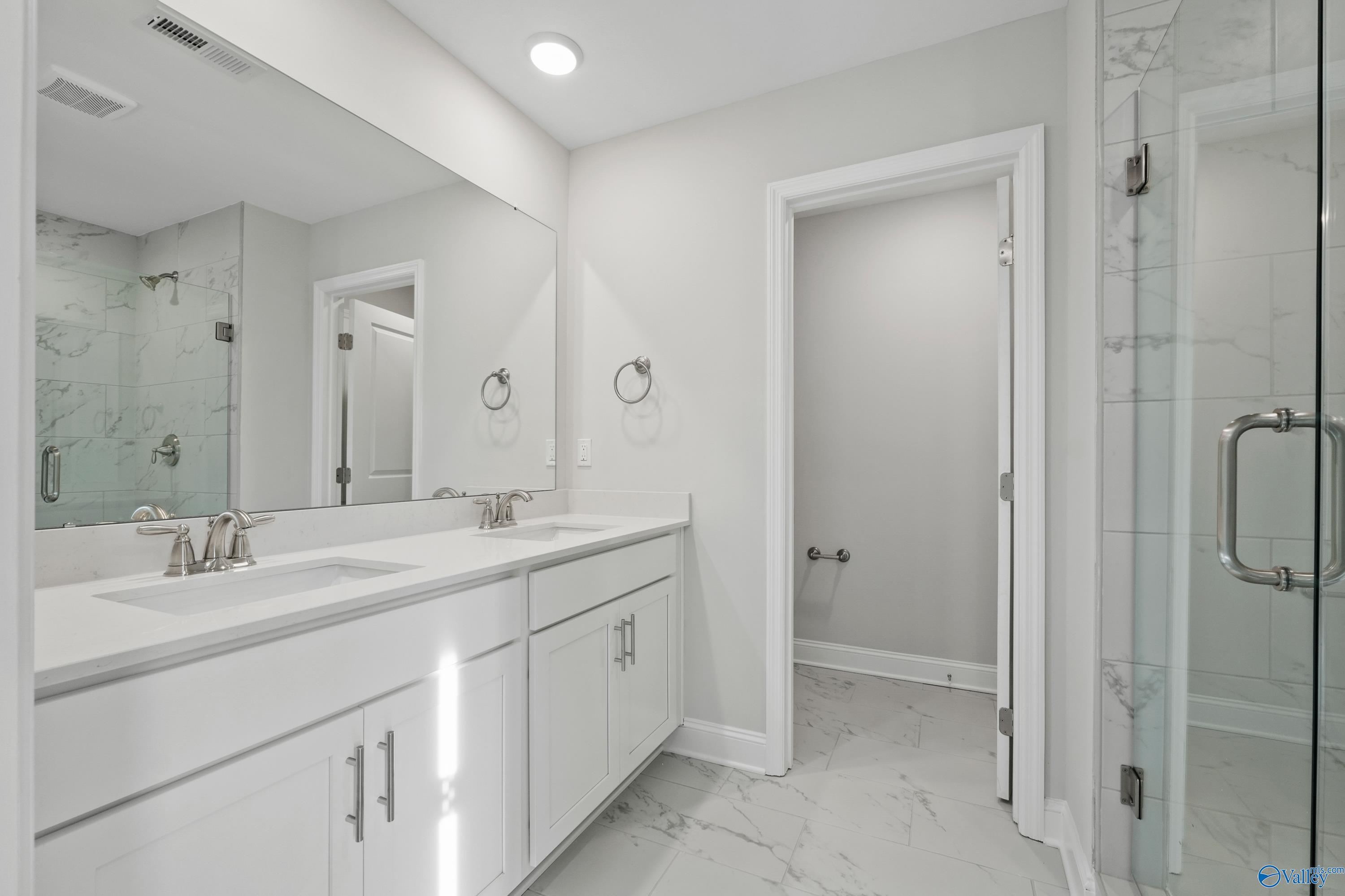 Modern master bathroom featuring double white vanity, frameless glass shower, and marble tile floors in Davidson Homes The Camden, Huntsville AL