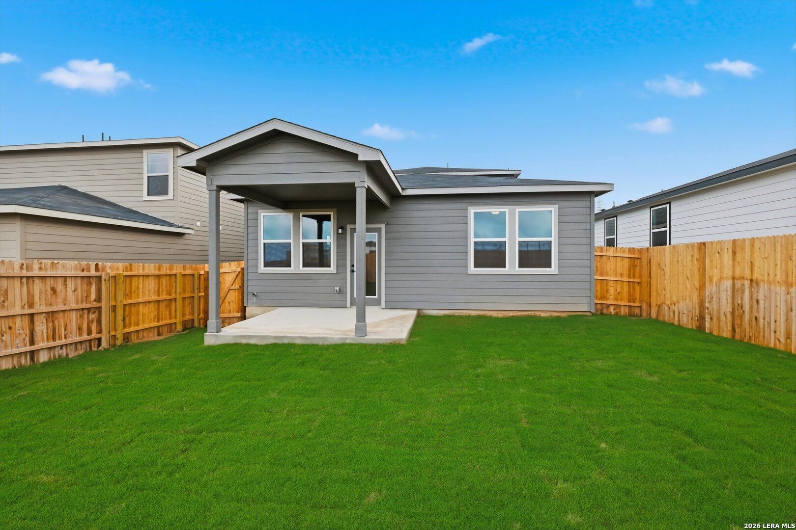 Back view of gray-sided 2-story home with covered patio, large windows, and lush green lawn in Agave, San Antonio, Texas - Davidson Homes The Blanco C