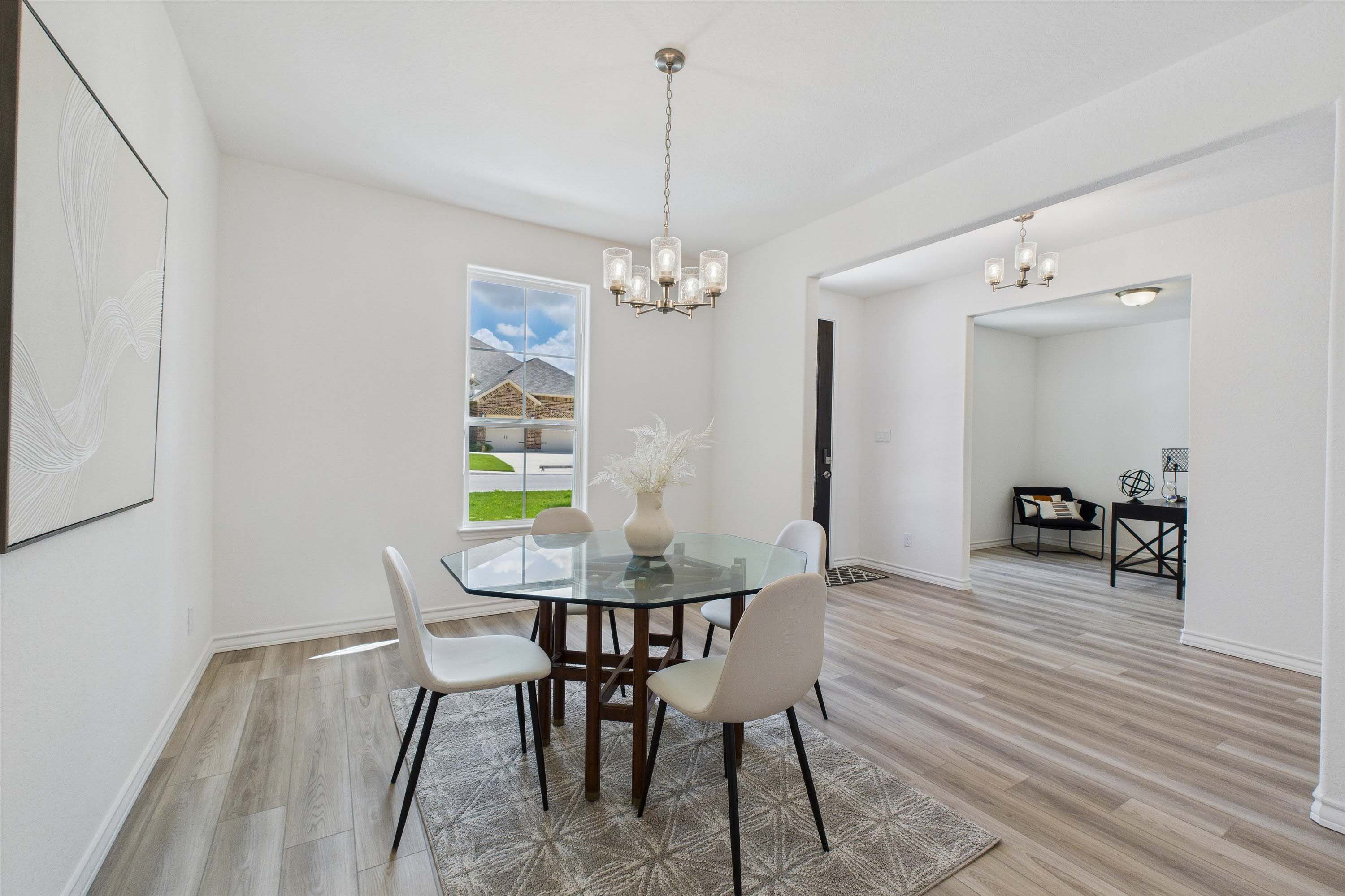 Bright dining area in The Danbury featuring a glass-top table, modern lighting, and wood-look flooring in Castroville, TX.