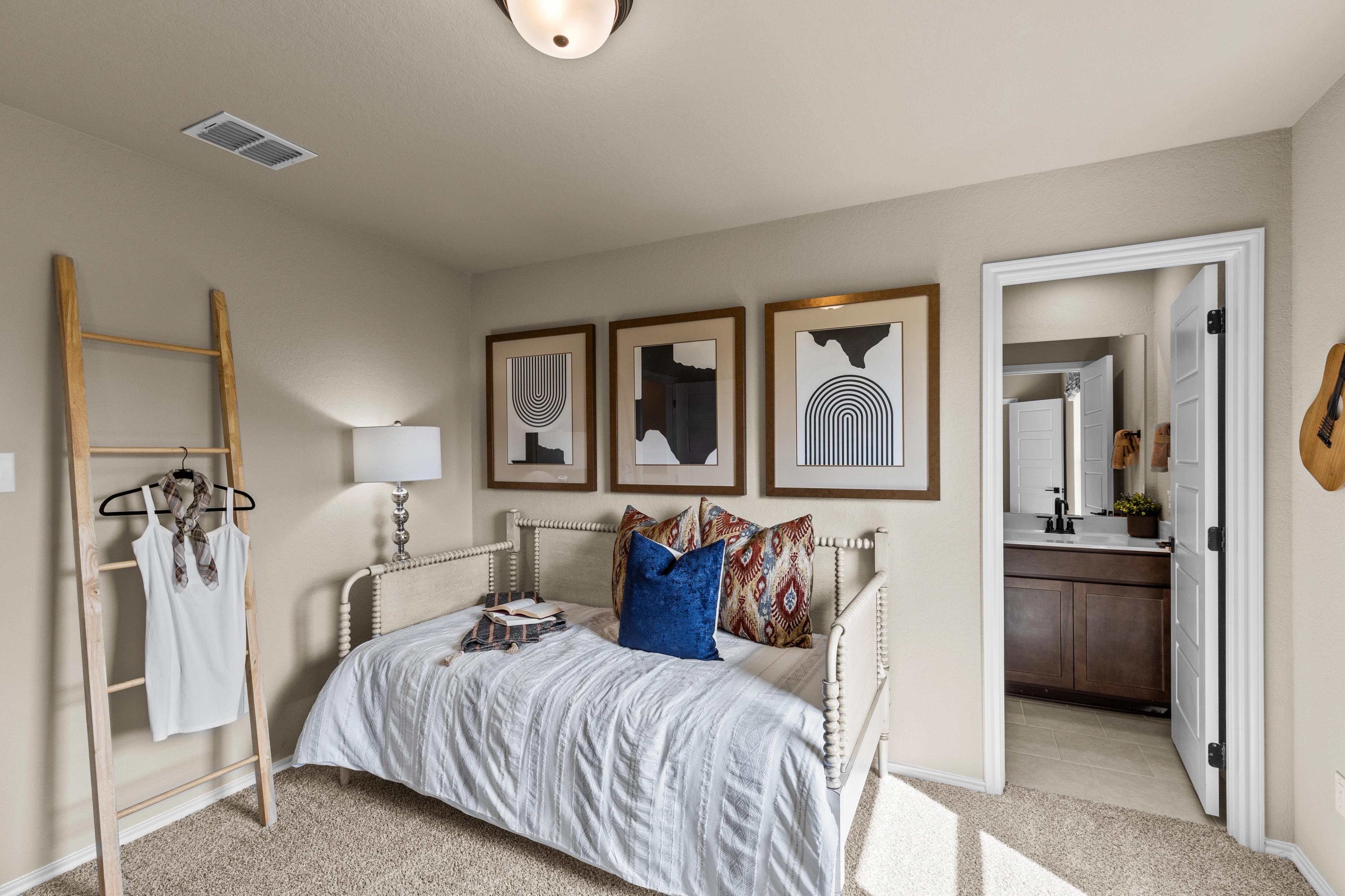 Cozy Bricewood bedroom in San Antonio TX by Davidson Homes with white trundle bed, abstract art, ladder shelf, and en-suite bath