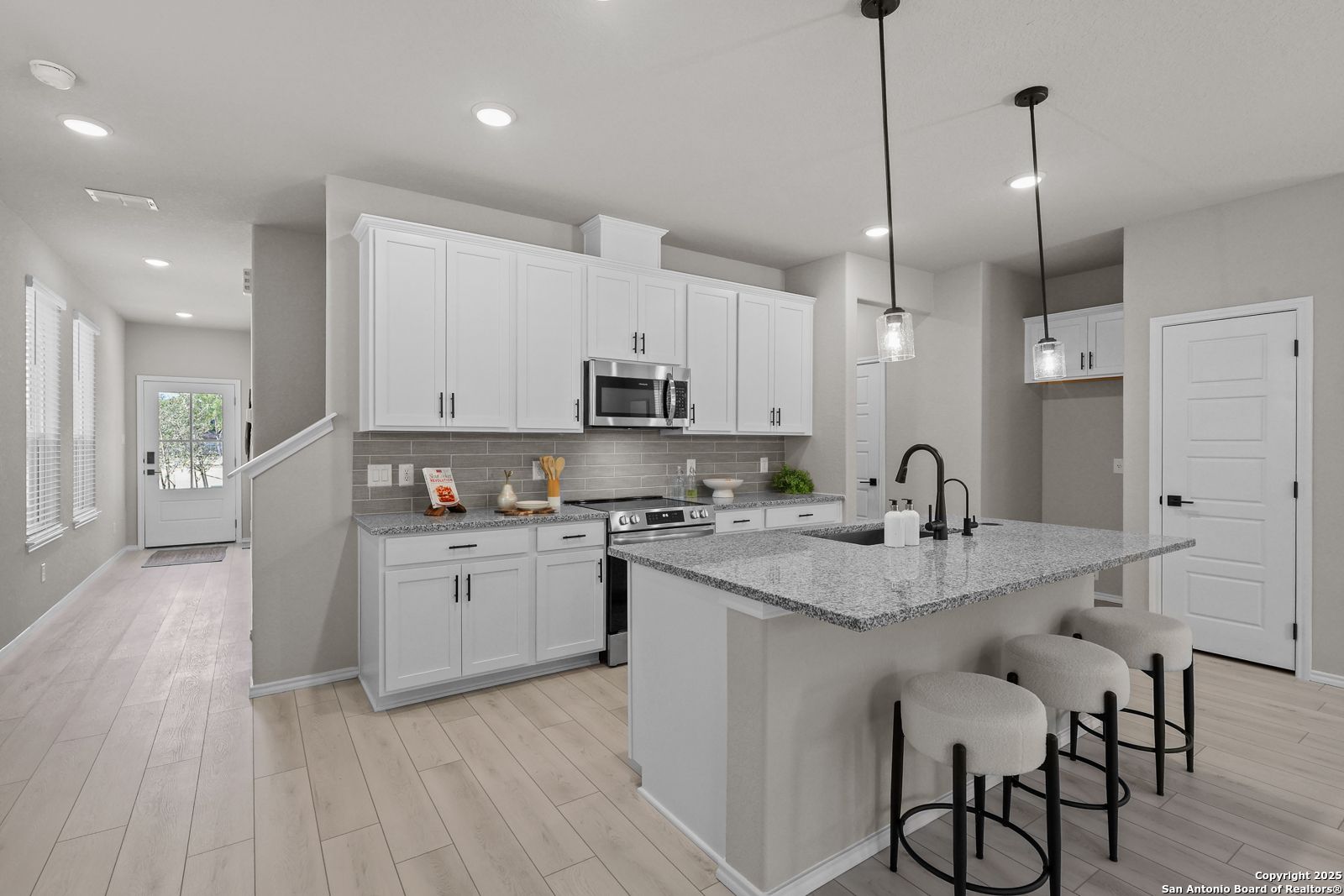 Modern white kitchen with granite island, stainless appliances, pendant lights in Davidson Homes The Charlotte B, San Antonio
