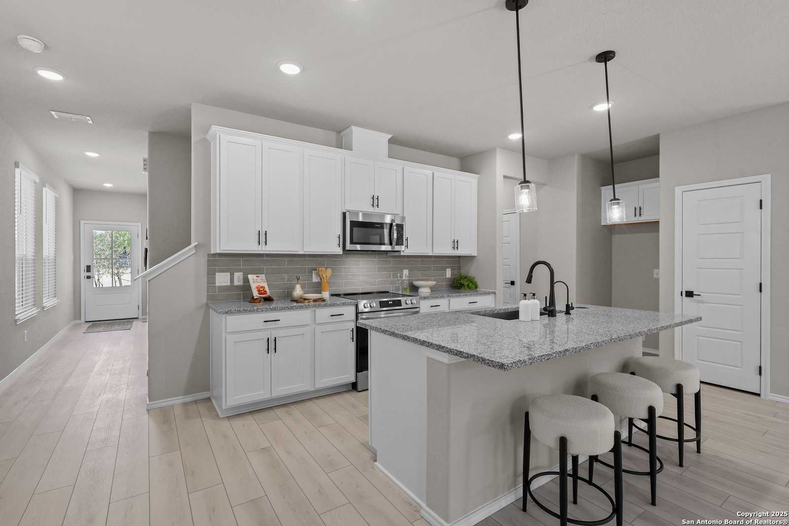 Modern white kitchen with granite island, stainless appliances, pendant lights in Davidson Homes The Charlotte B, San Antonio