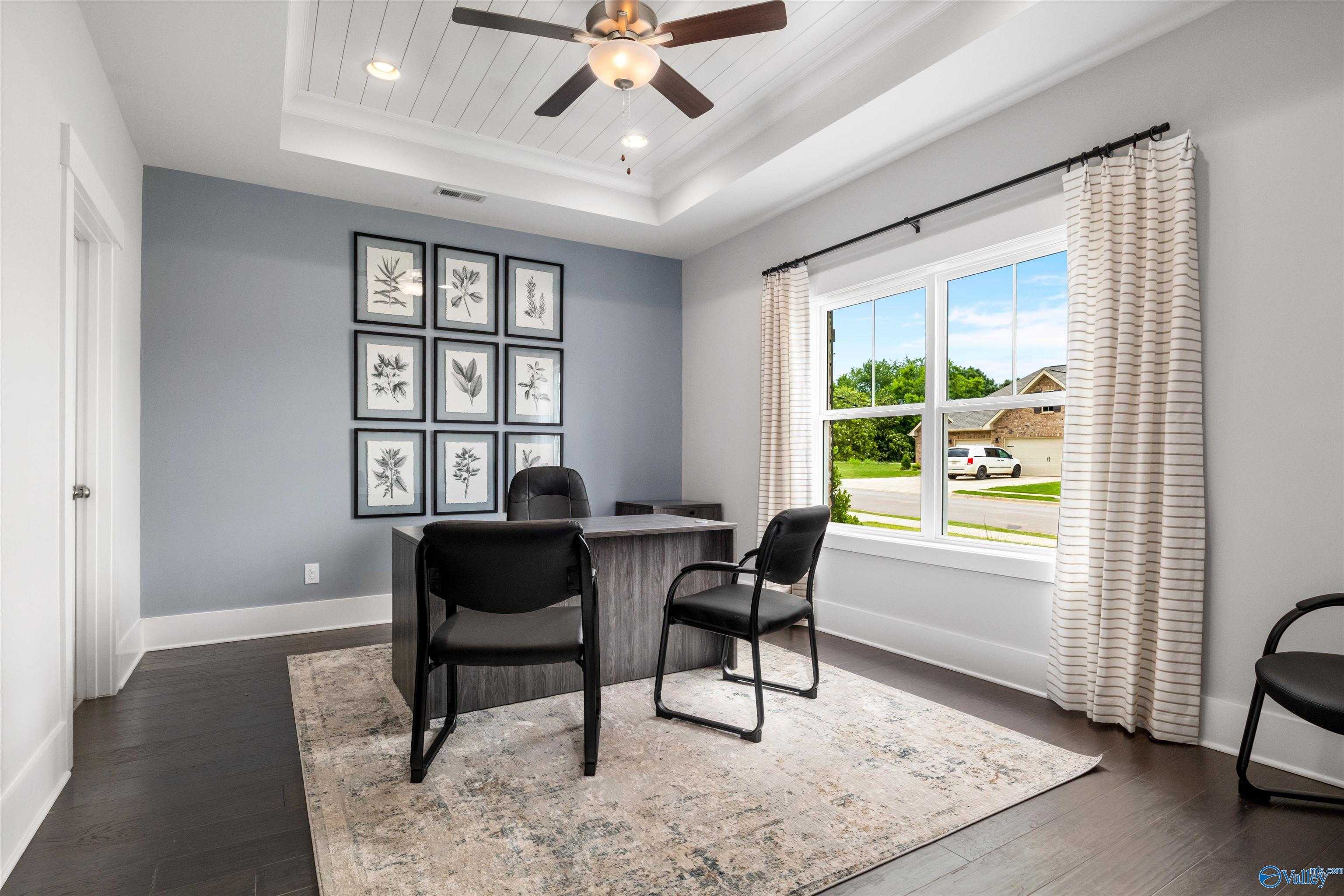 Cozy home office with gray walls, botanical art, desk, chairs, ceiling fan, and window view in Davidson Homes The Covington C, Decatur, AL
