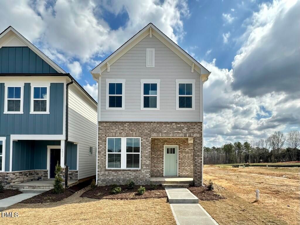 Modern 3-story gray siding home with brick base, green door, and brick walkway in Forestville Yard, Knightdale, NC by Davidson Homes The Burke