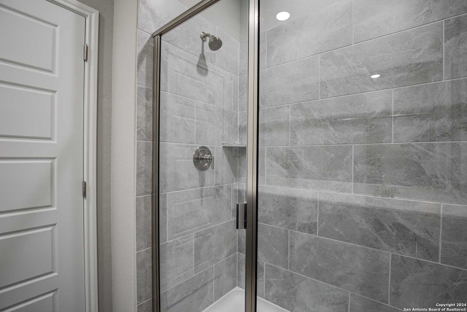 Modern frameless glass shower with gray subway tile walls and niche shelf in The Frio B master bath, San Antonio, Texas