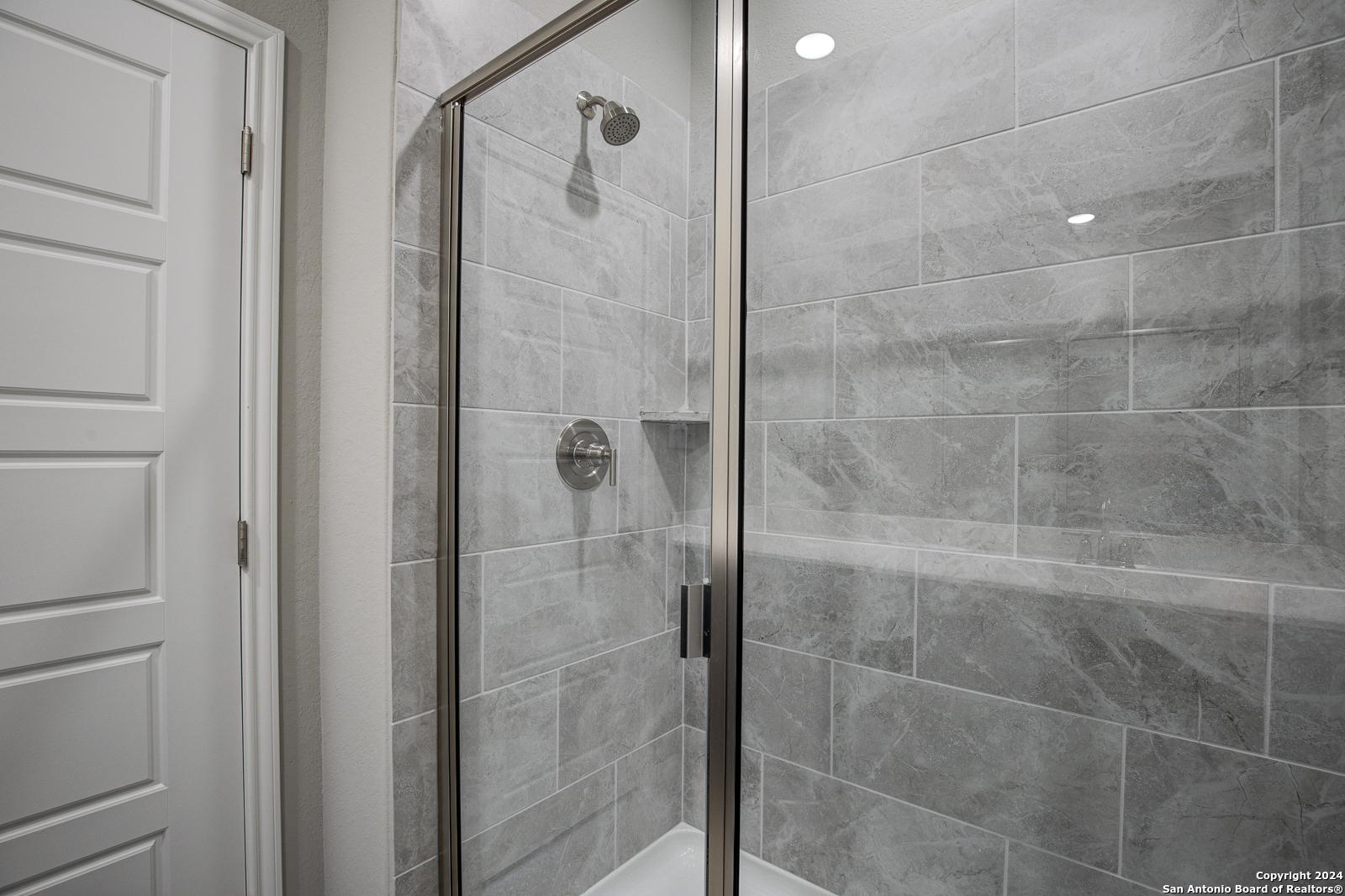 Modern frameless glass shower with gray subway tile walls and niche shelf in The Frio B master bath, San Antonio, Texas